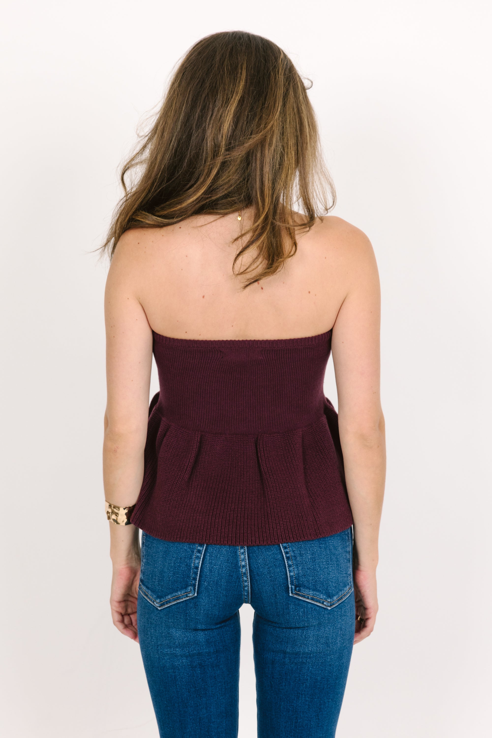 Woman wearing a strapless cranberry top and blue jeans on a plain background