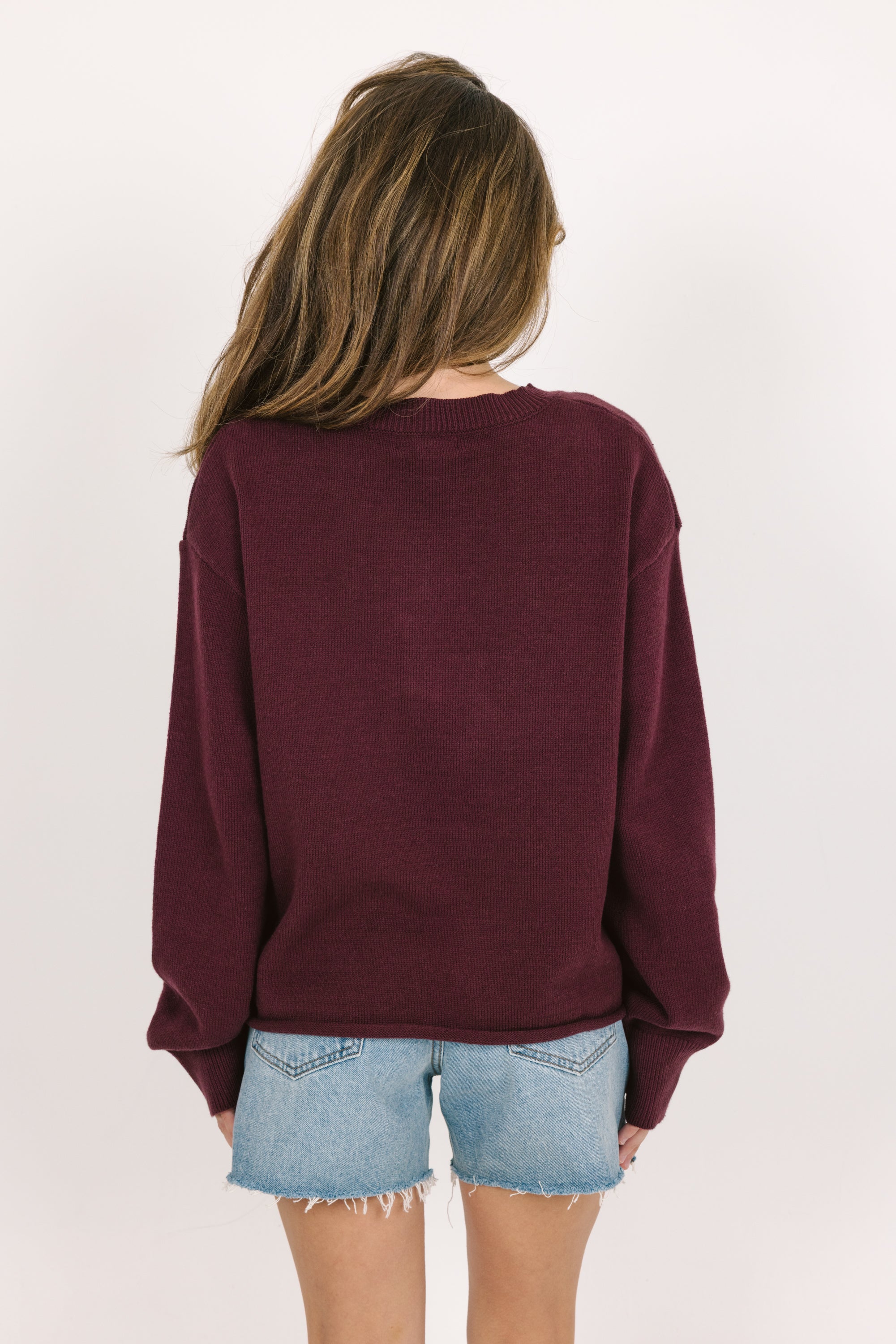 Person wearing a cranberry sweater and denim shorts on a plain background