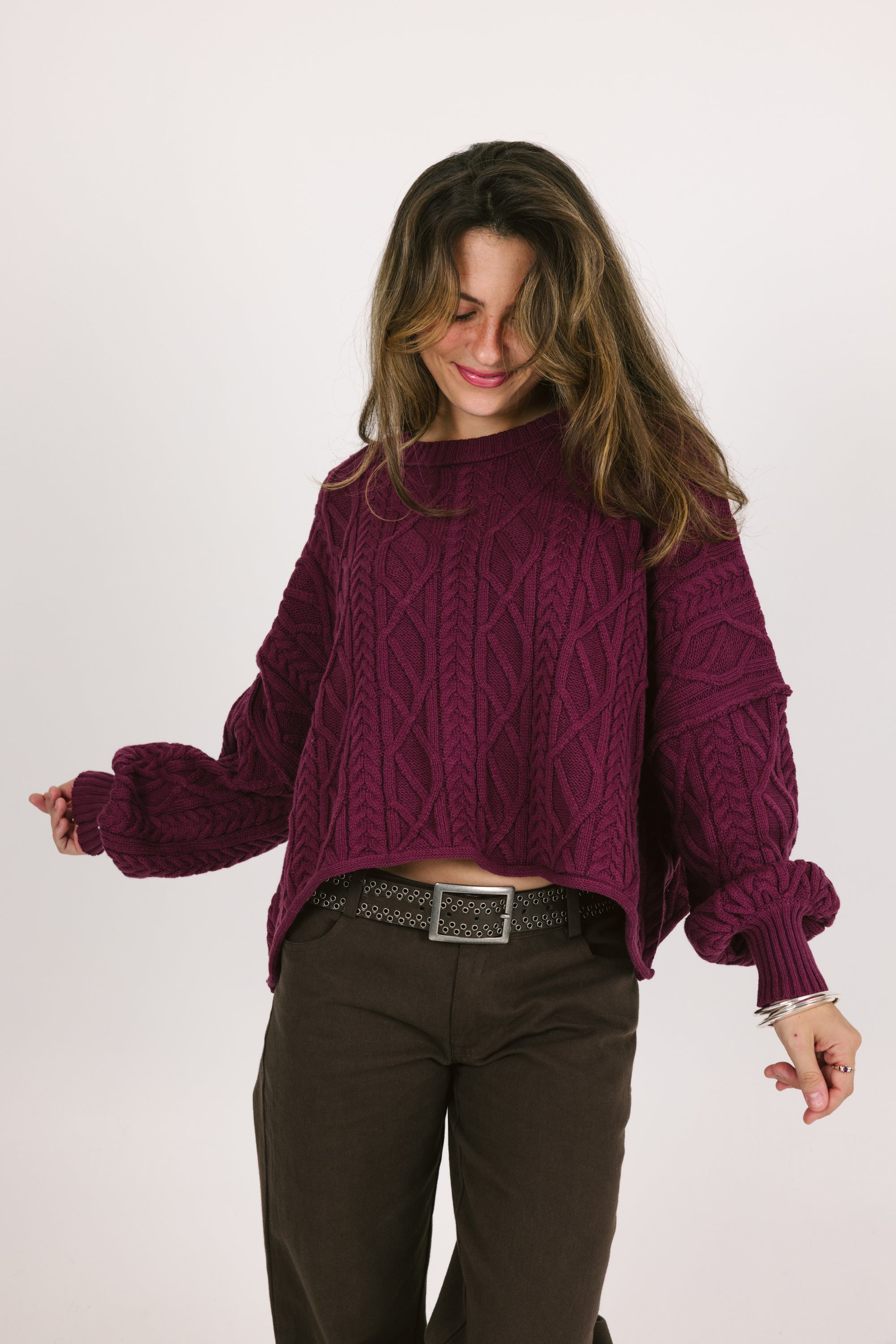 Woman wearing a purple cable knit sweater and brown pants on a white background