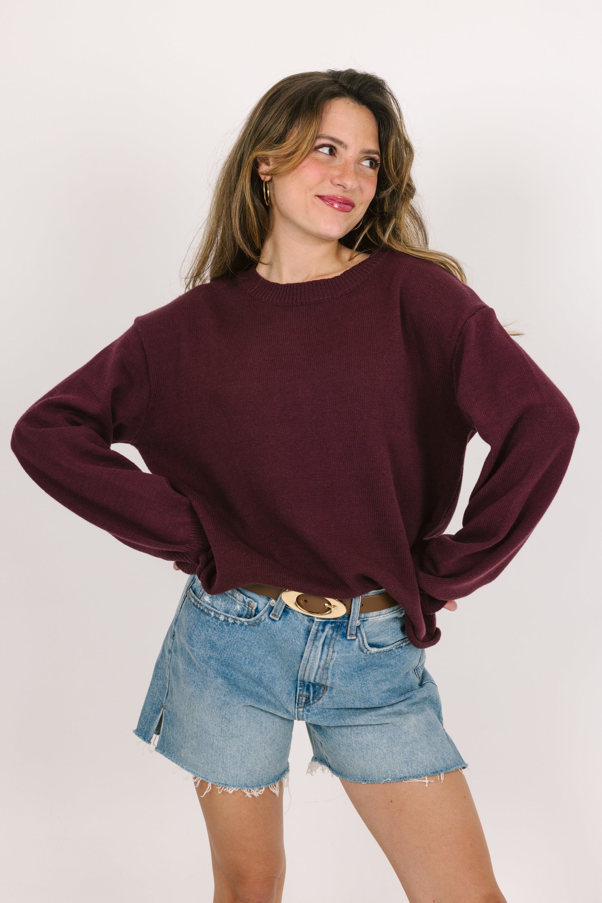 Person wearing a cranberry sweater and denim shorts on a plain background