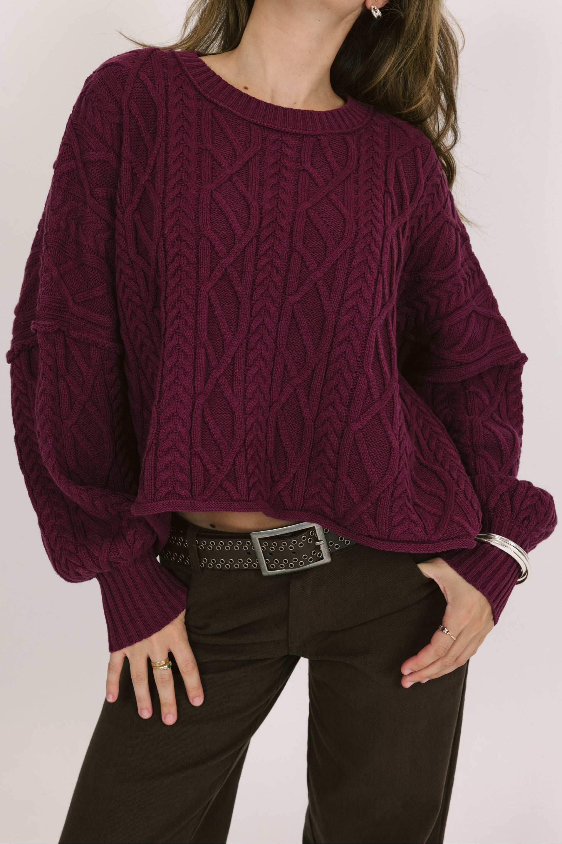 Person wearing a purple cable knit sweater with a plain background