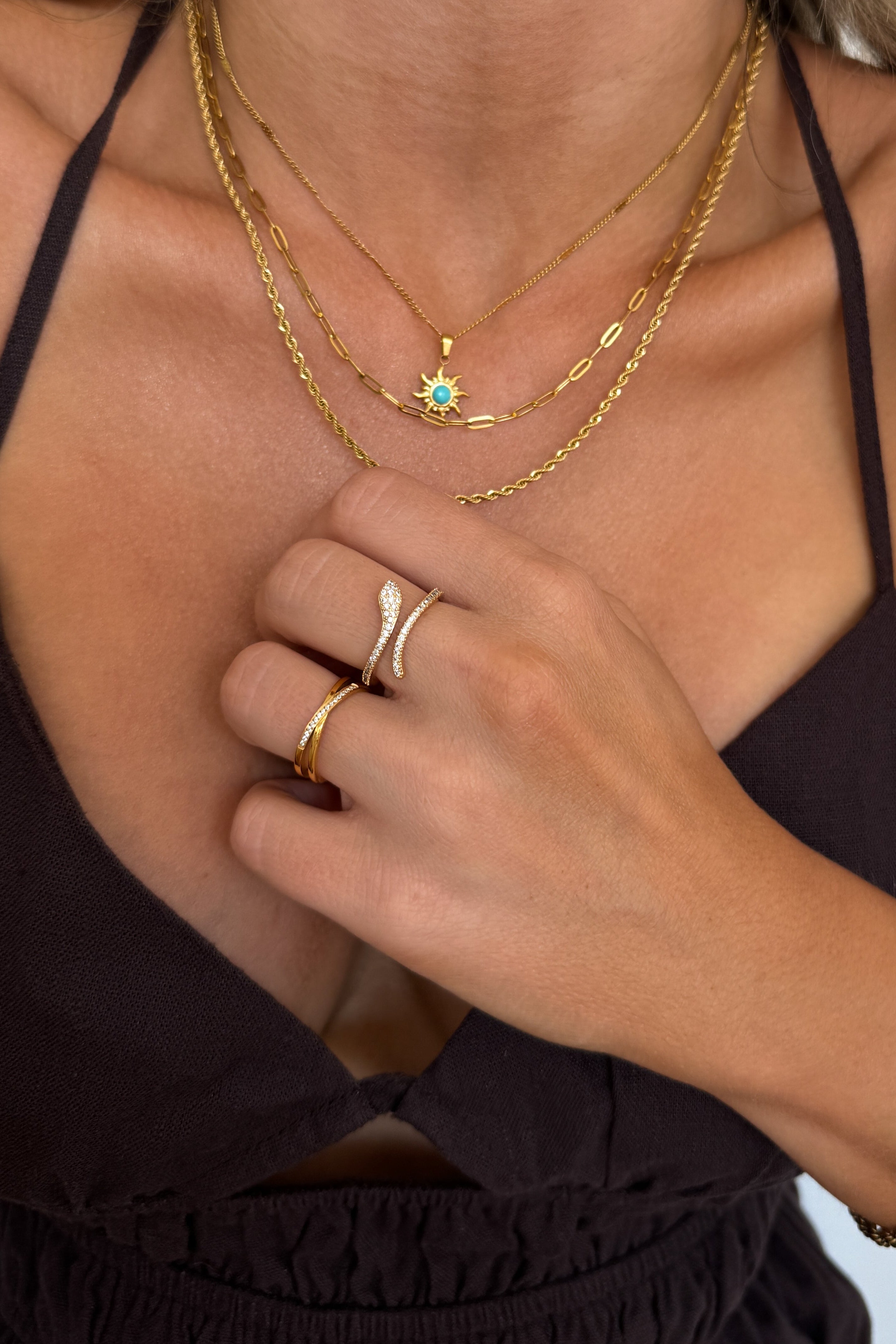 Close-up of a person wearing gold jewelry including necklaces, rings, and a bracelet.