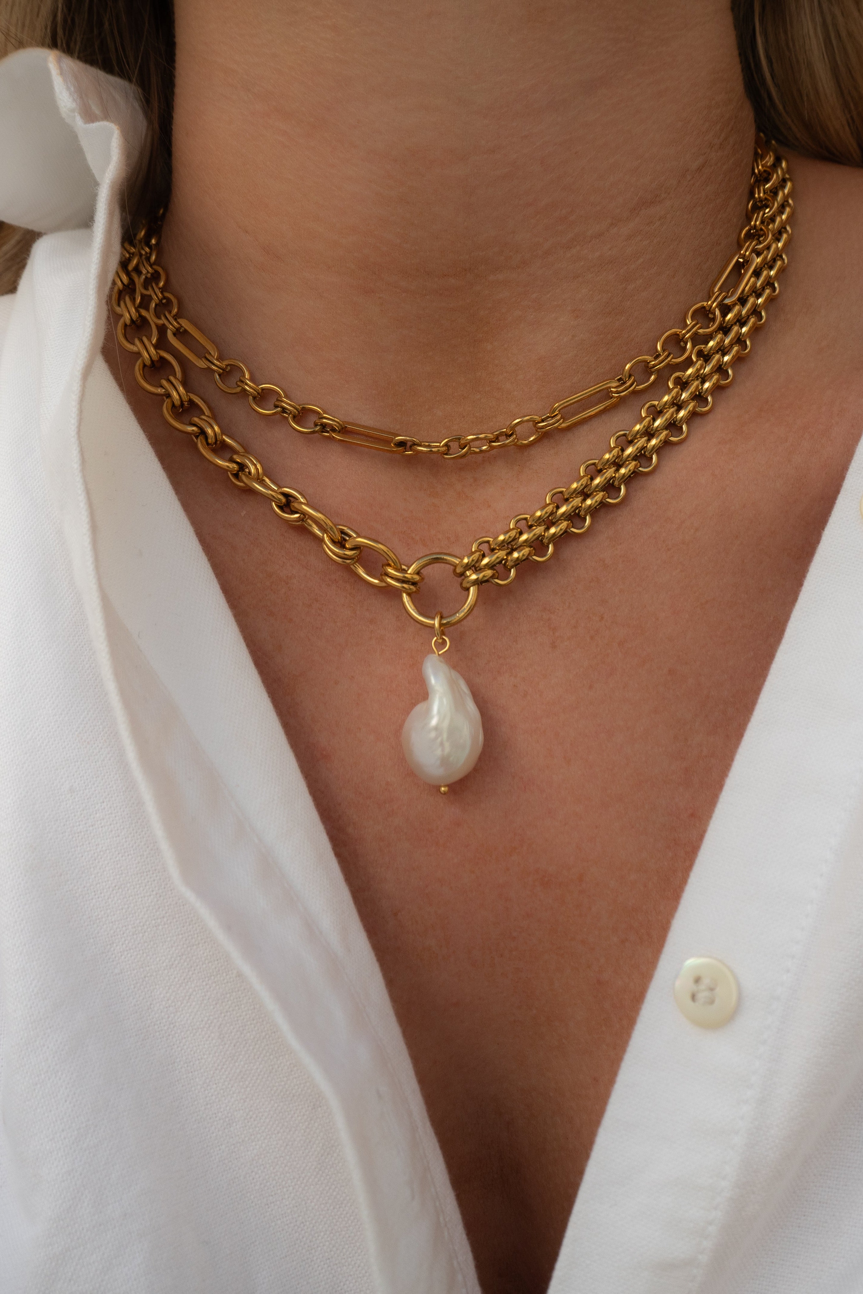 Gold chain necklace with a pearl pendant worn by a person in a white shirt.