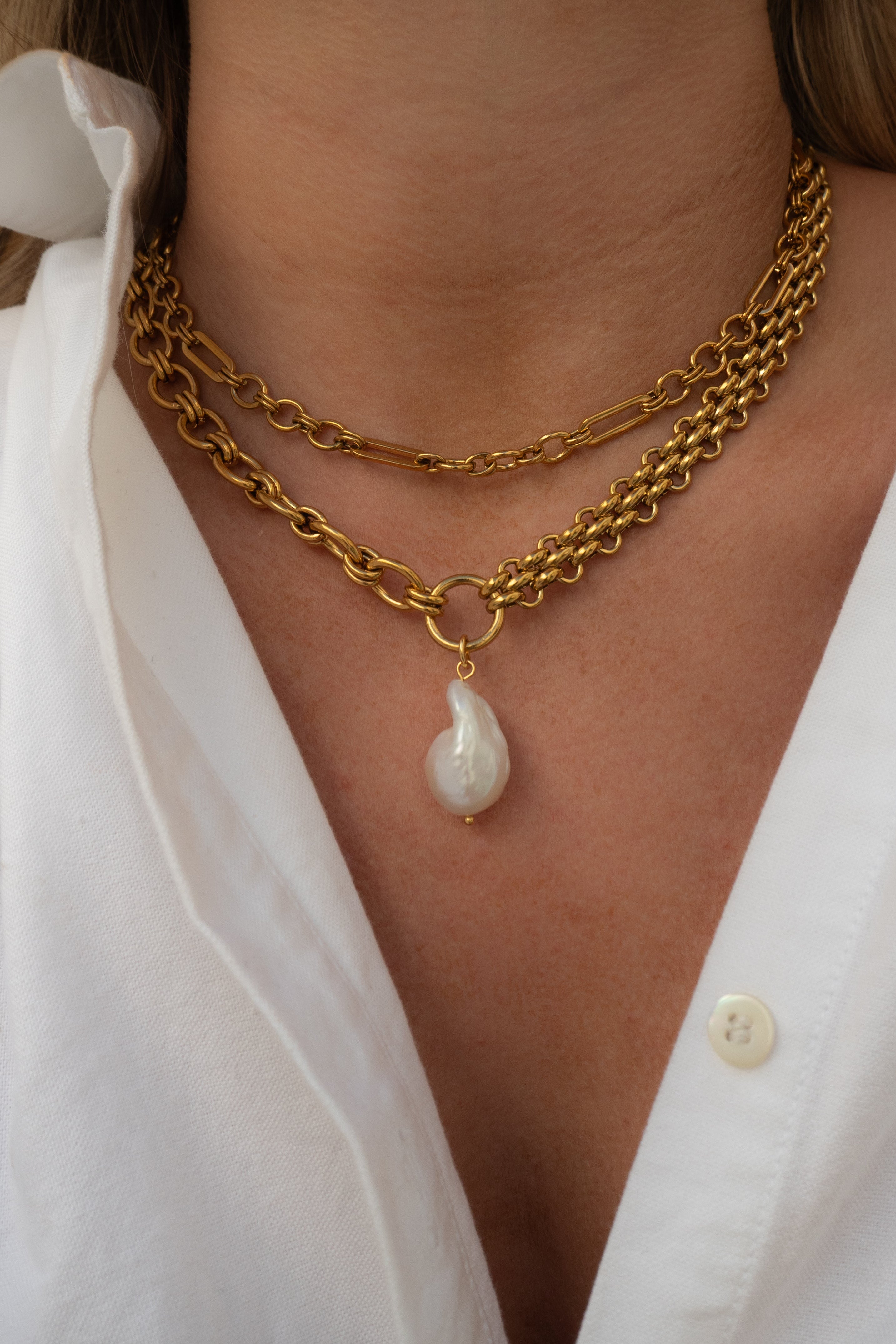 Gold chain necklace with a pearl pendant worn by a person in a white shirt.