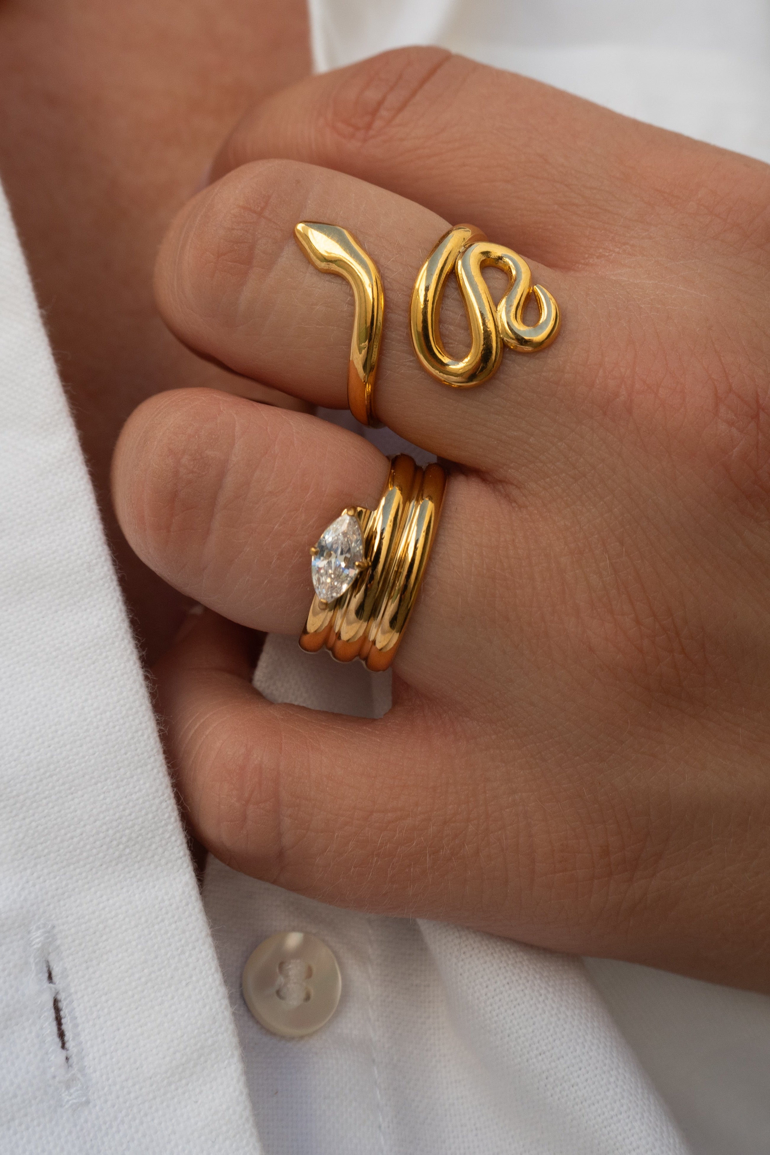 Hand wearing gold rings with a white shirt background