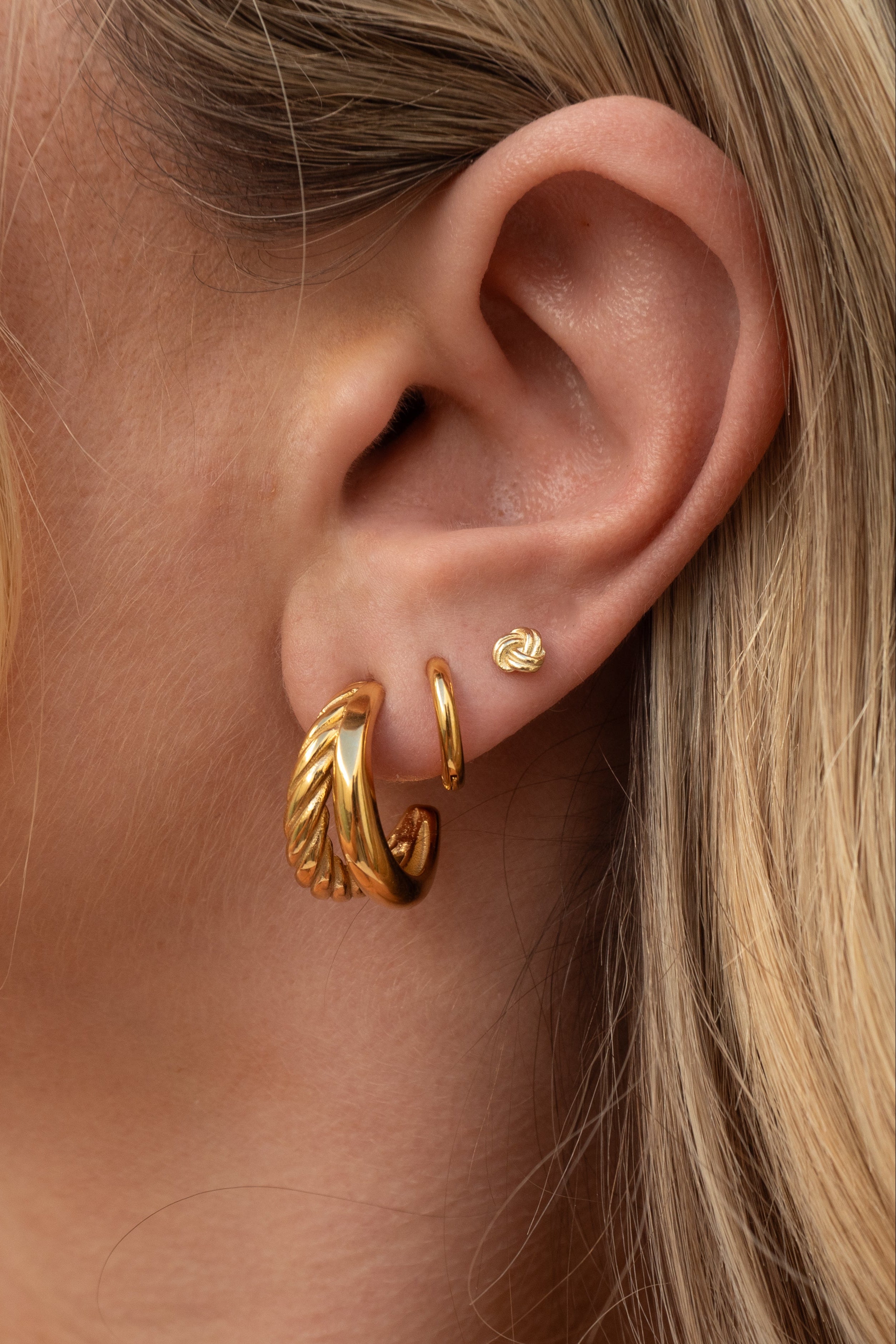 Close-up of a person wearing gold hoop earrings with blonde hair.