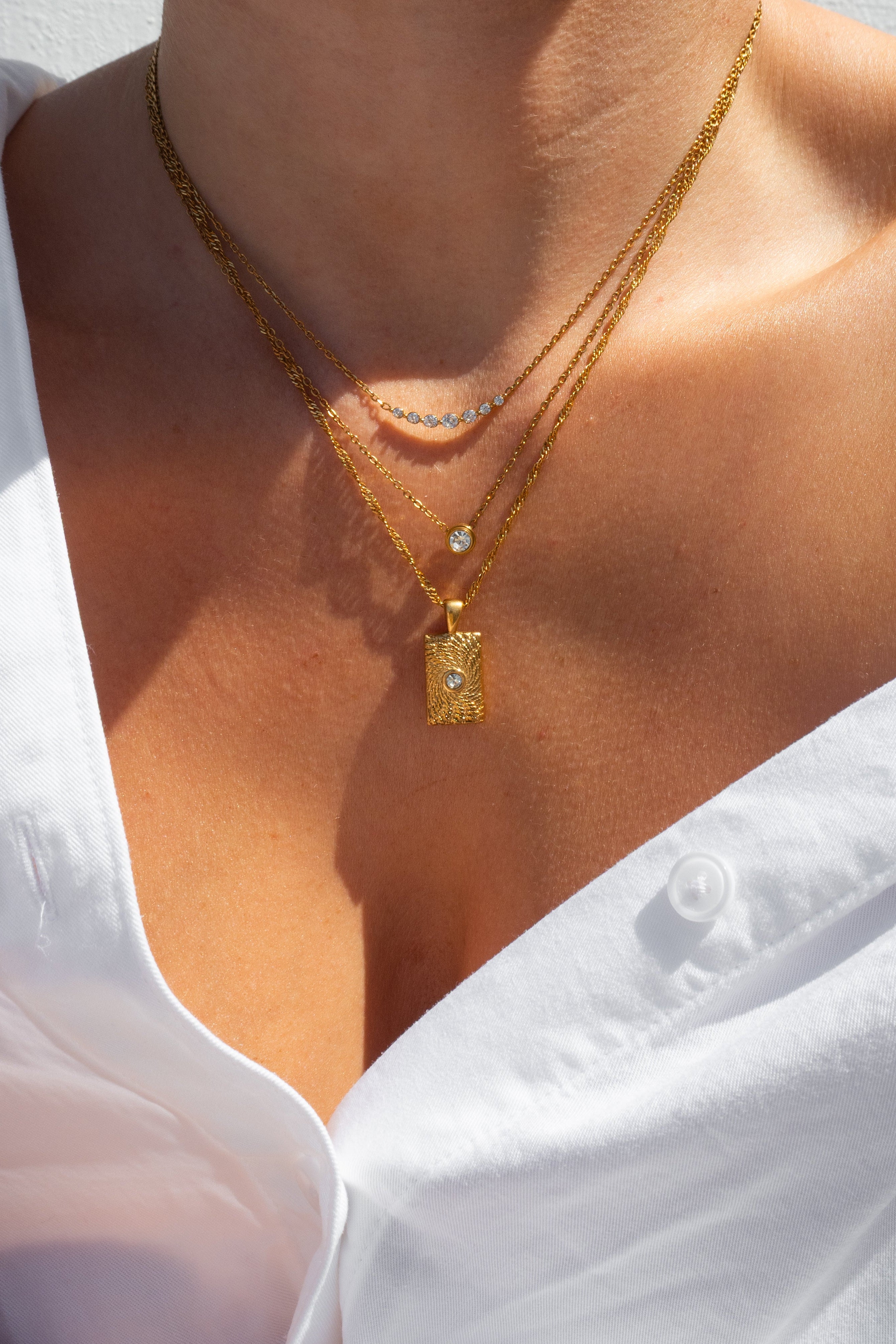 Close-up of a person wearing gold necklaces with a white shirt.