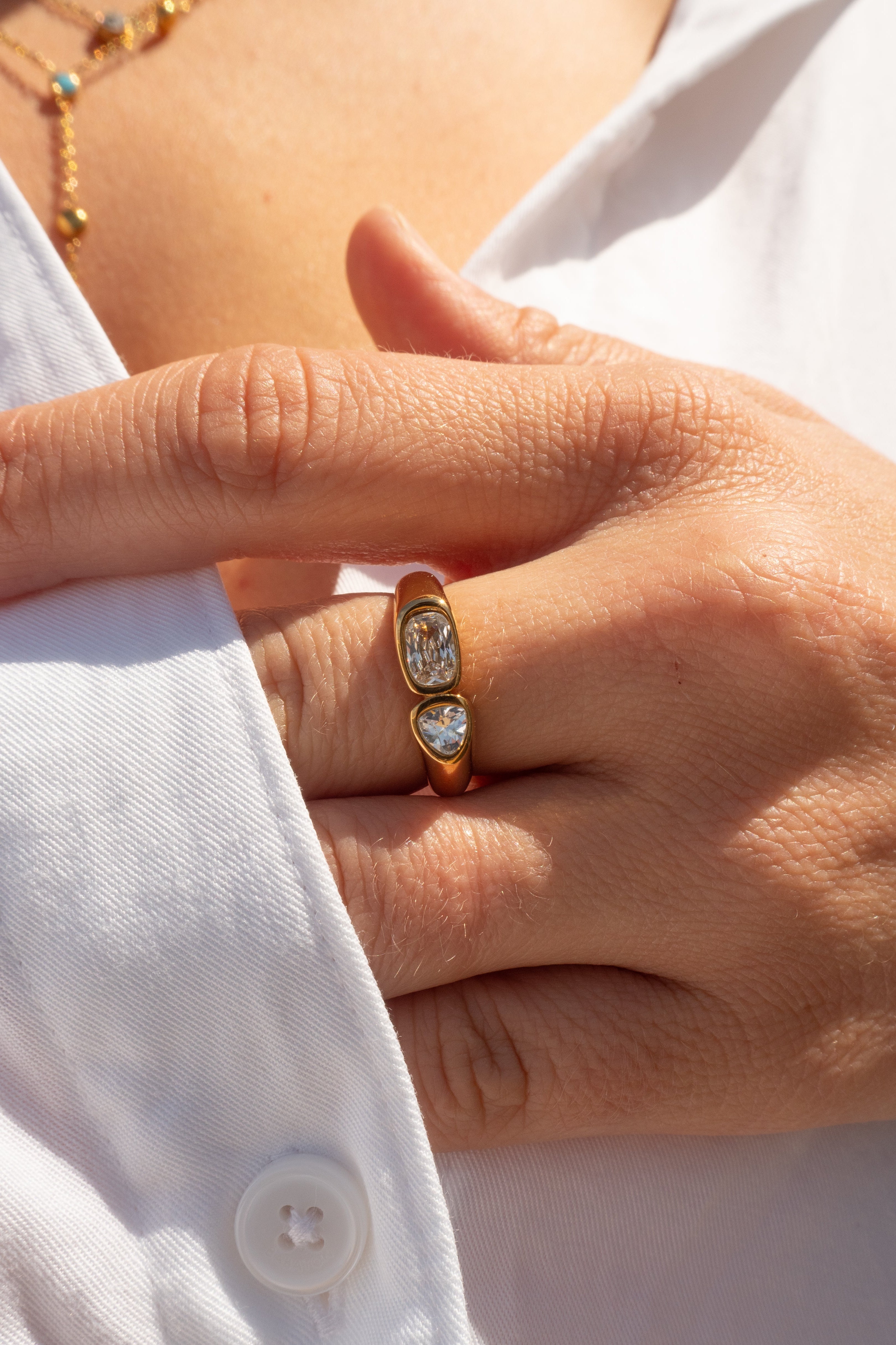 Close-up of a hand wearing a gold ring with a diamond on a white shirt background