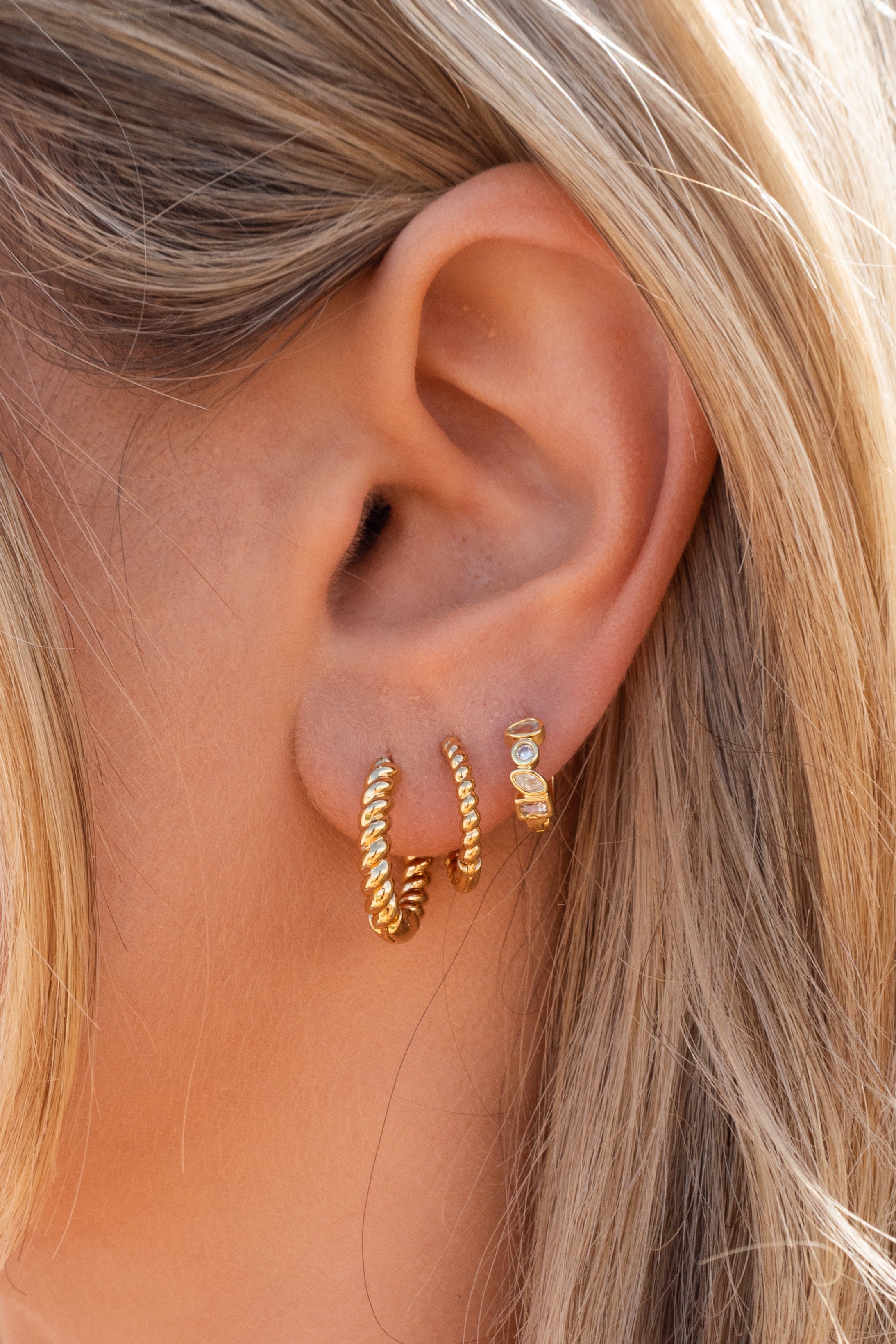 Close-up of an ear wearing gold hoop earrings with blonde hair.