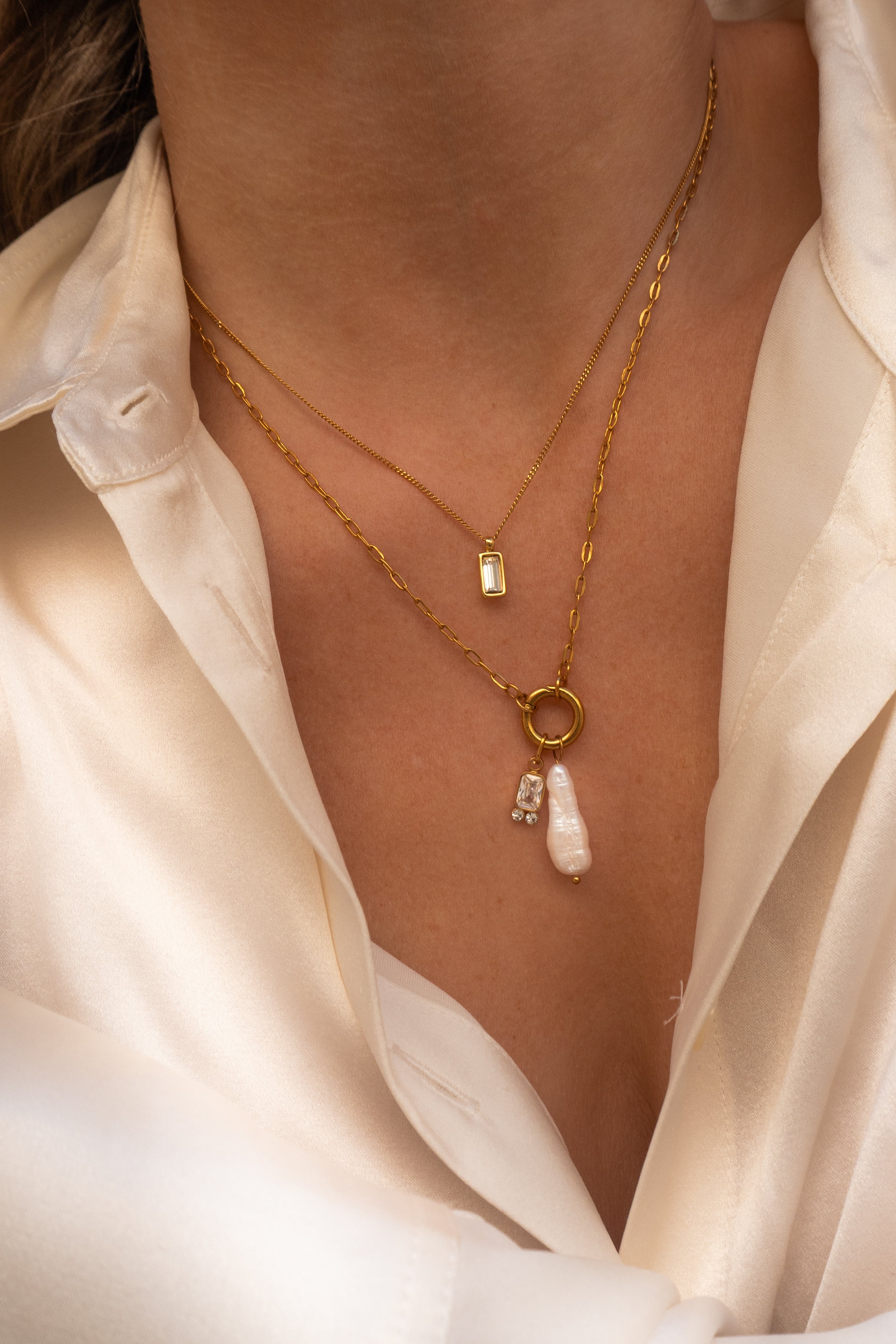 Gold necklace with a pearl pendant worn by a person in a white shirt.