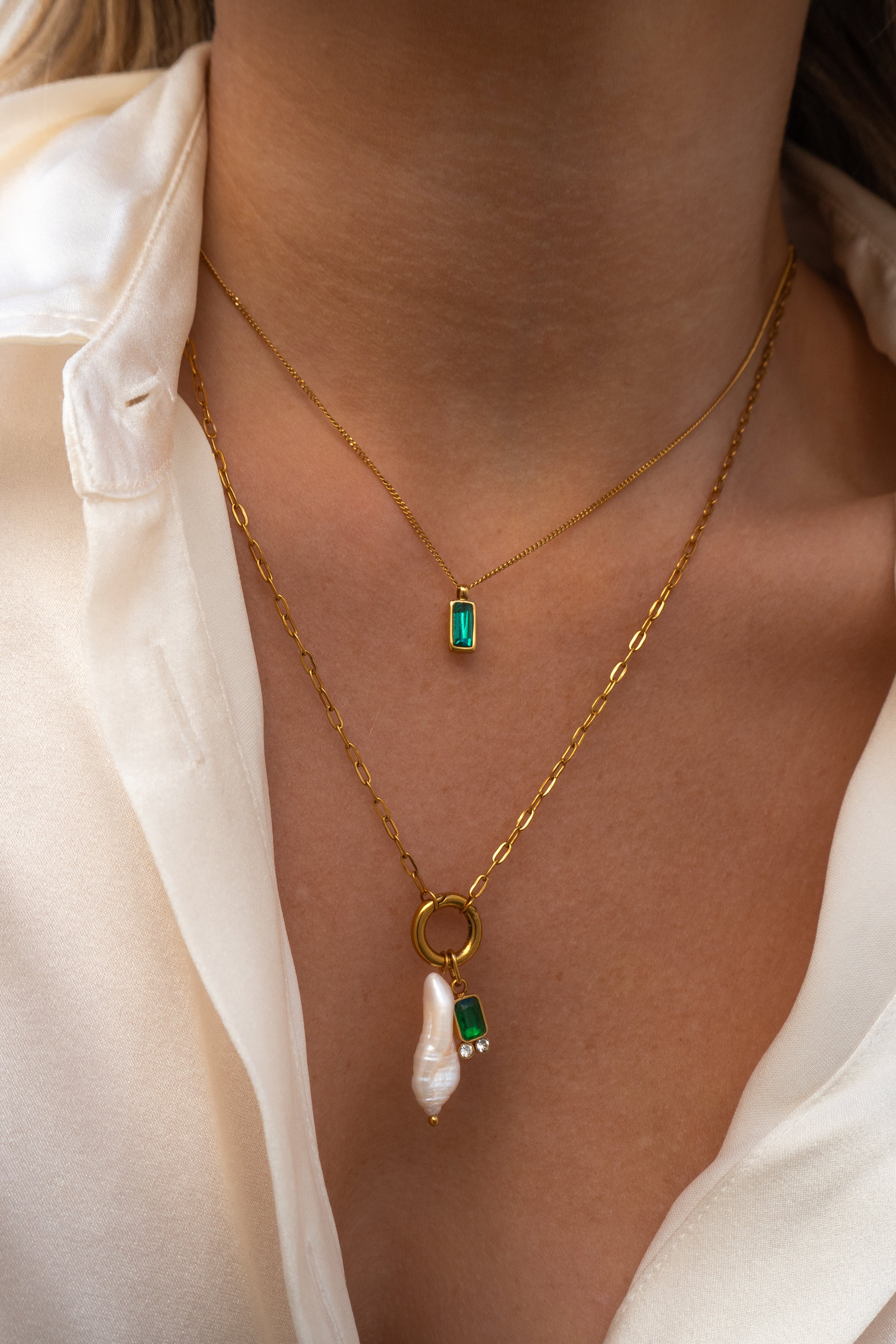 Gold necklace with green gemstones worn by a person against a neutral background