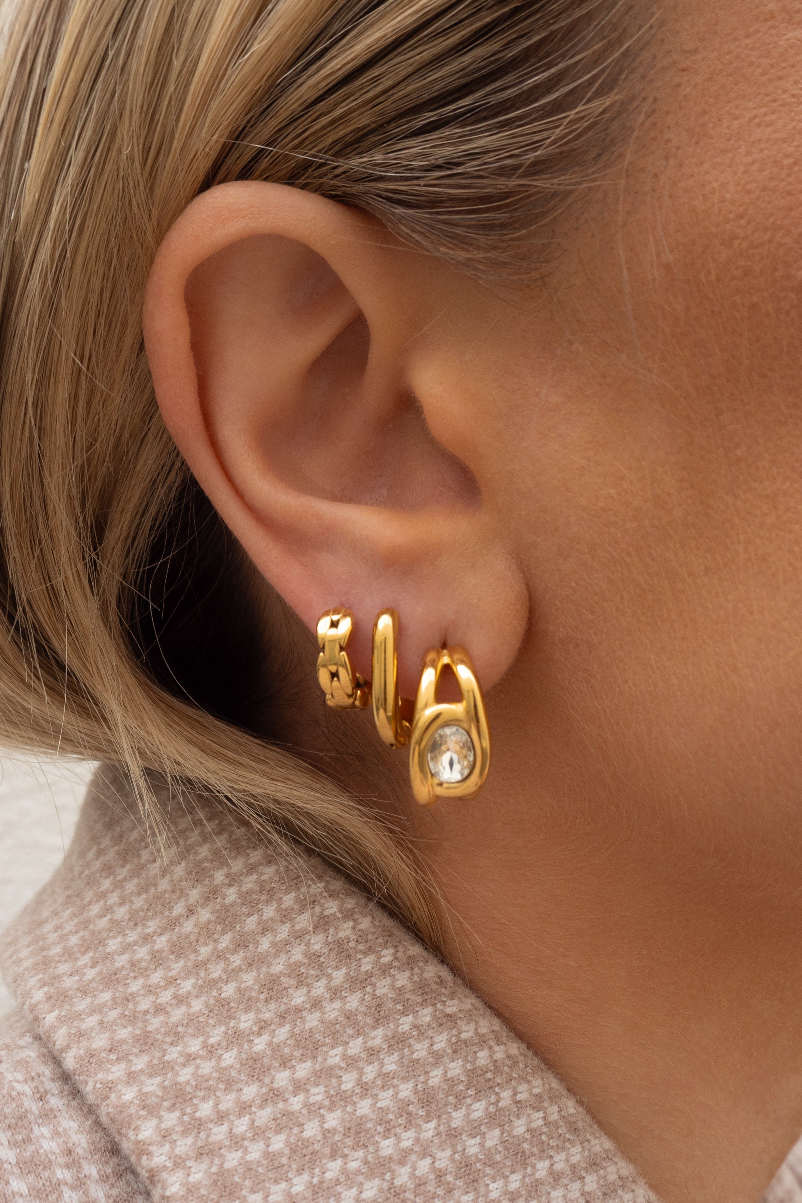 Close-up of an ear wearing gold hoop earrings with a neutral background