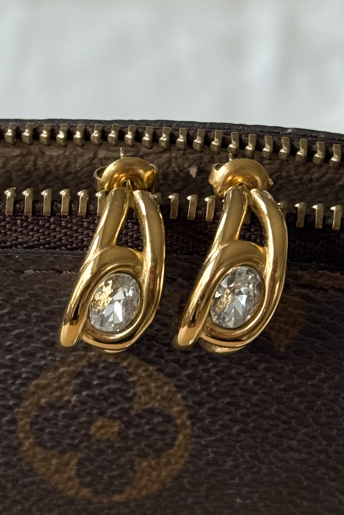 Gold hoop earrings with clear gemstones on a brown textured surface.