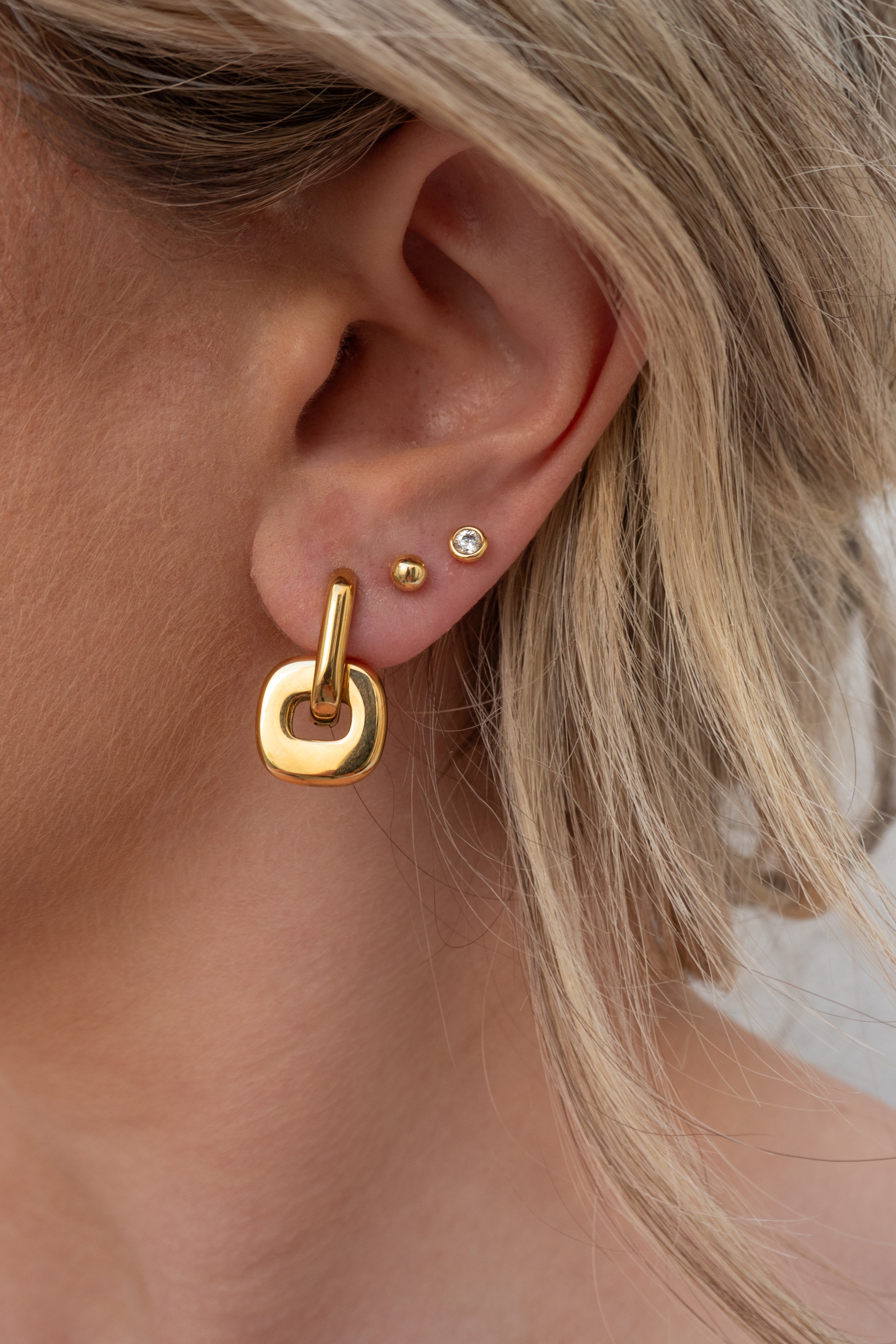 Close-up of a person wearing gold hoop earrings with a blurred background