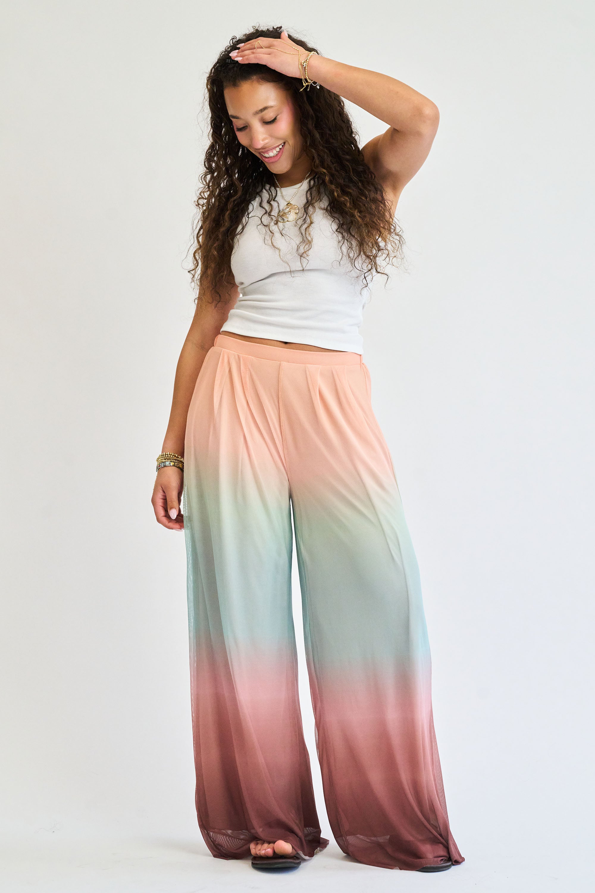 Woman wearing a white top and colorful ombre pants on a plain background
