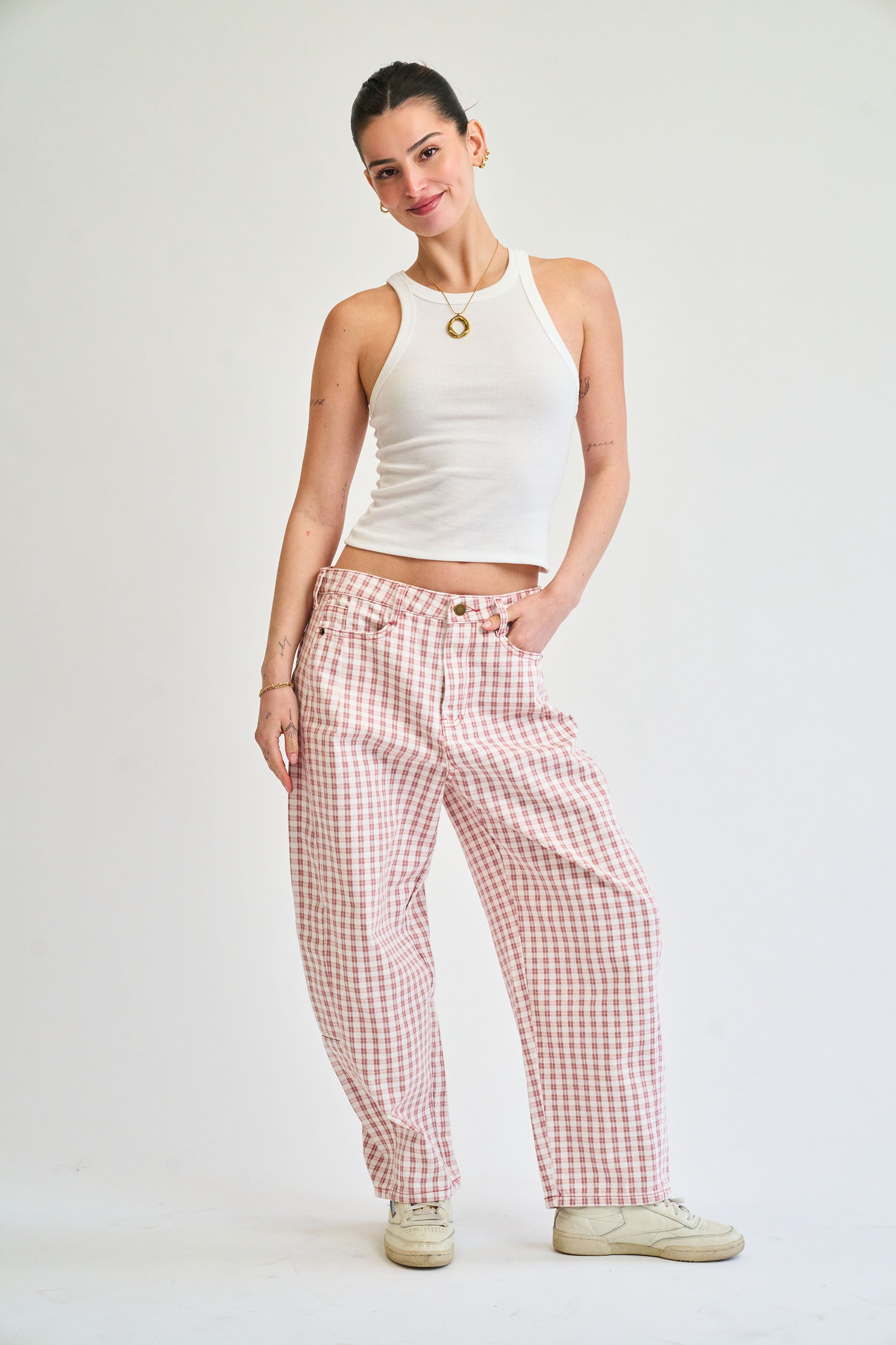 Woman wearing a white tank top and red checkered pants on a plain background