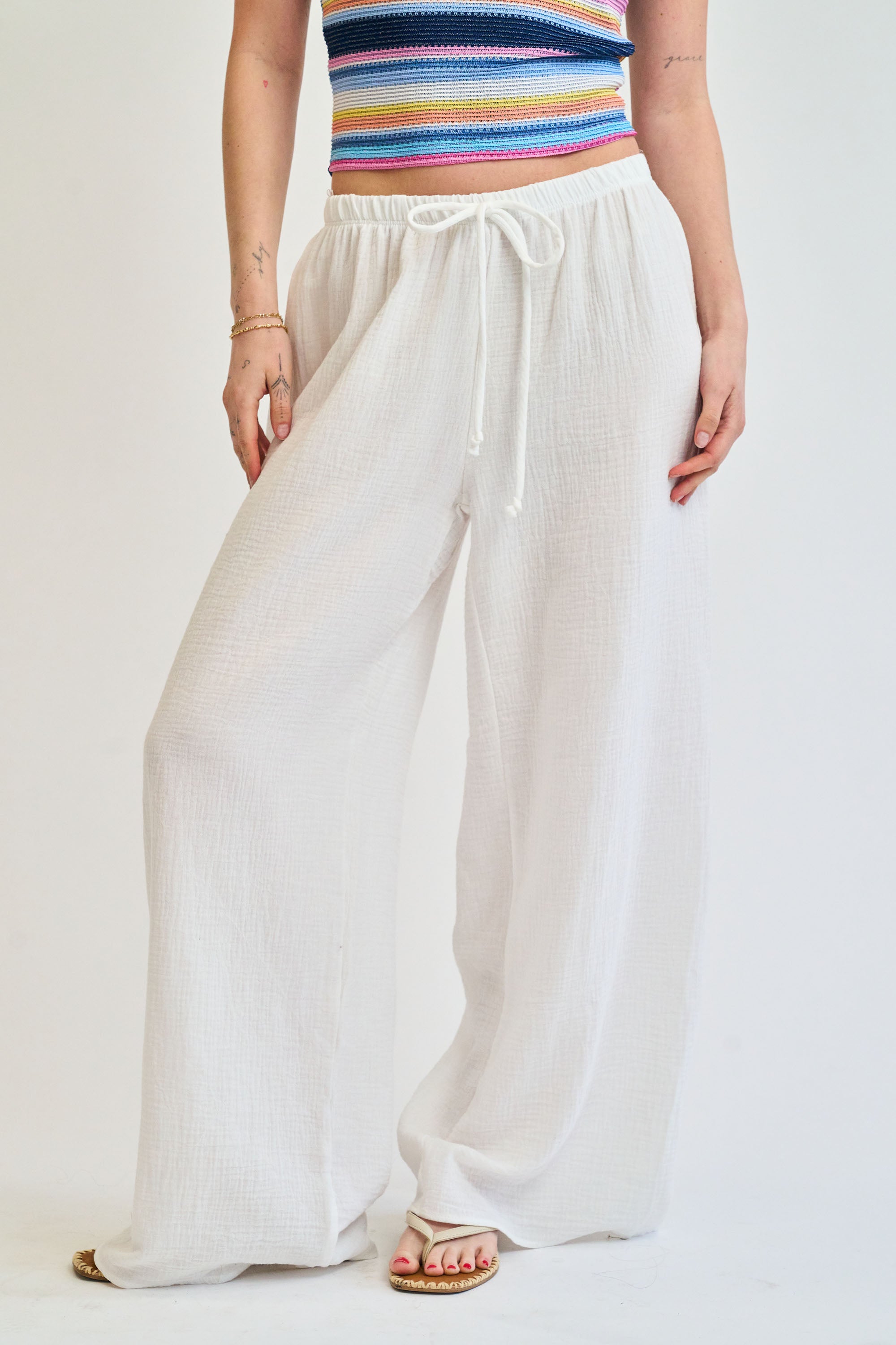 Person wearing a colorful striped top and white wide-leg pants on a plain background