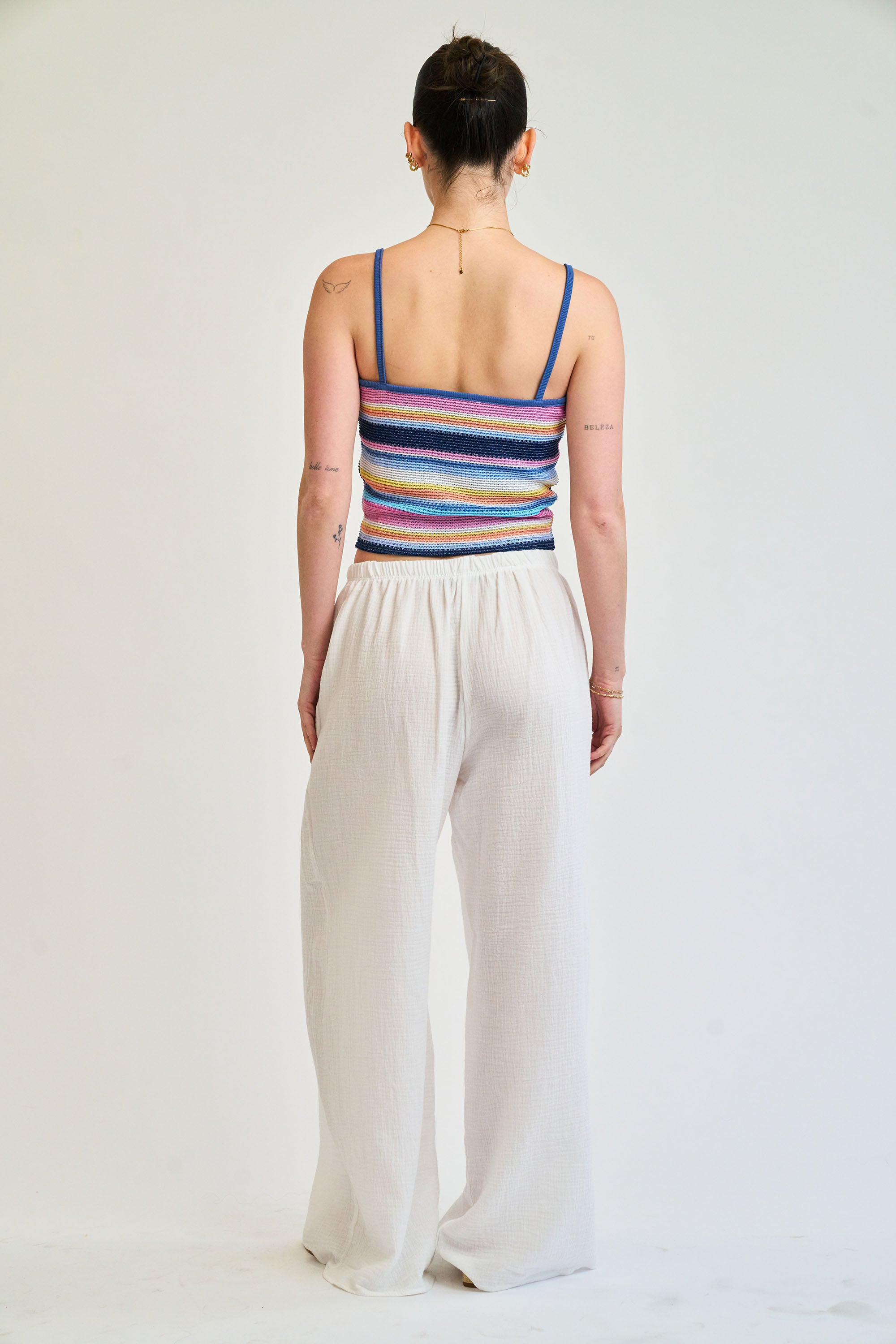 Person wearing a colorful striped tank top and white pants on a plain background