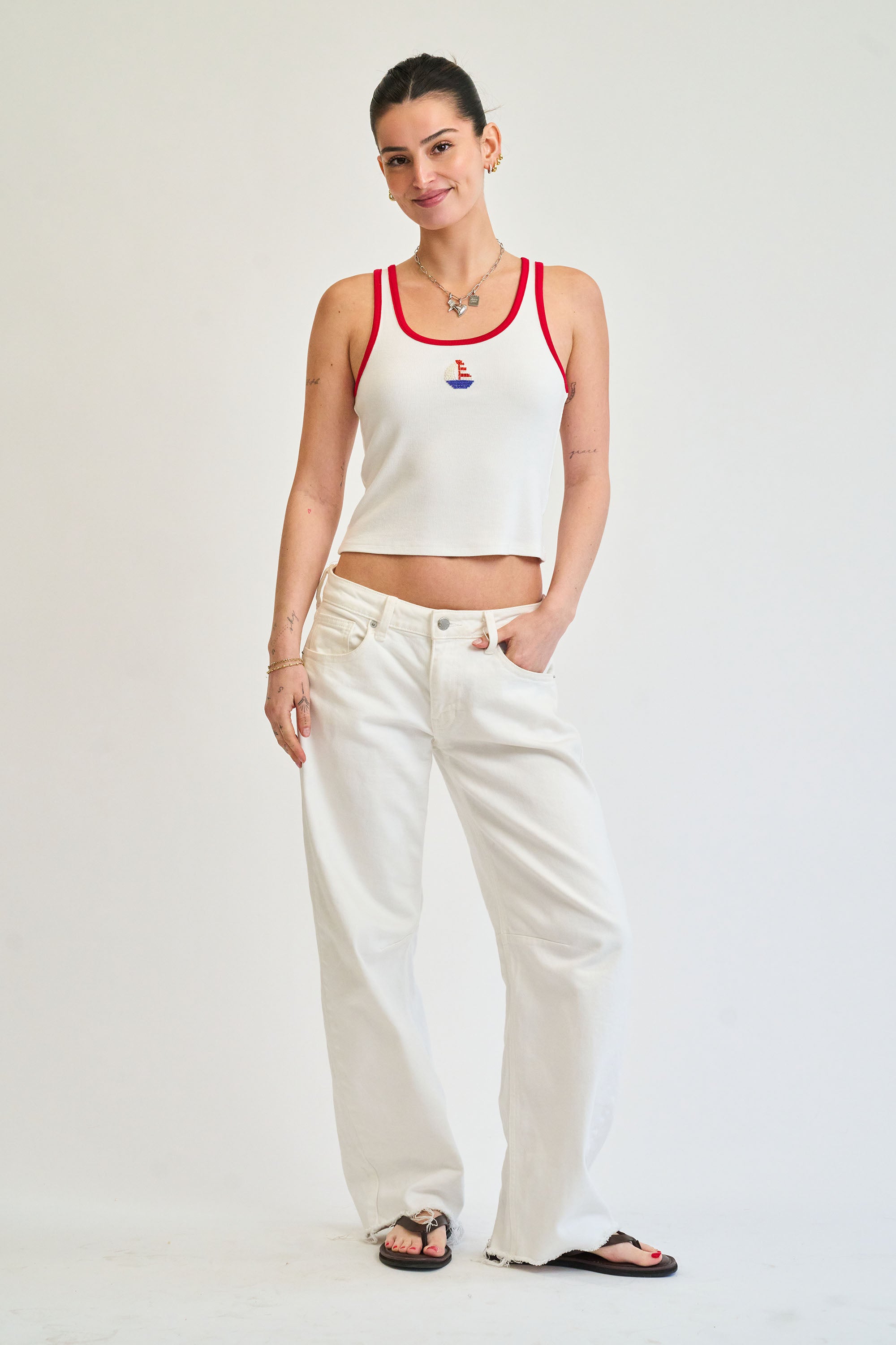 Woman wearing a white tank top with red trim and white pants on a plain background