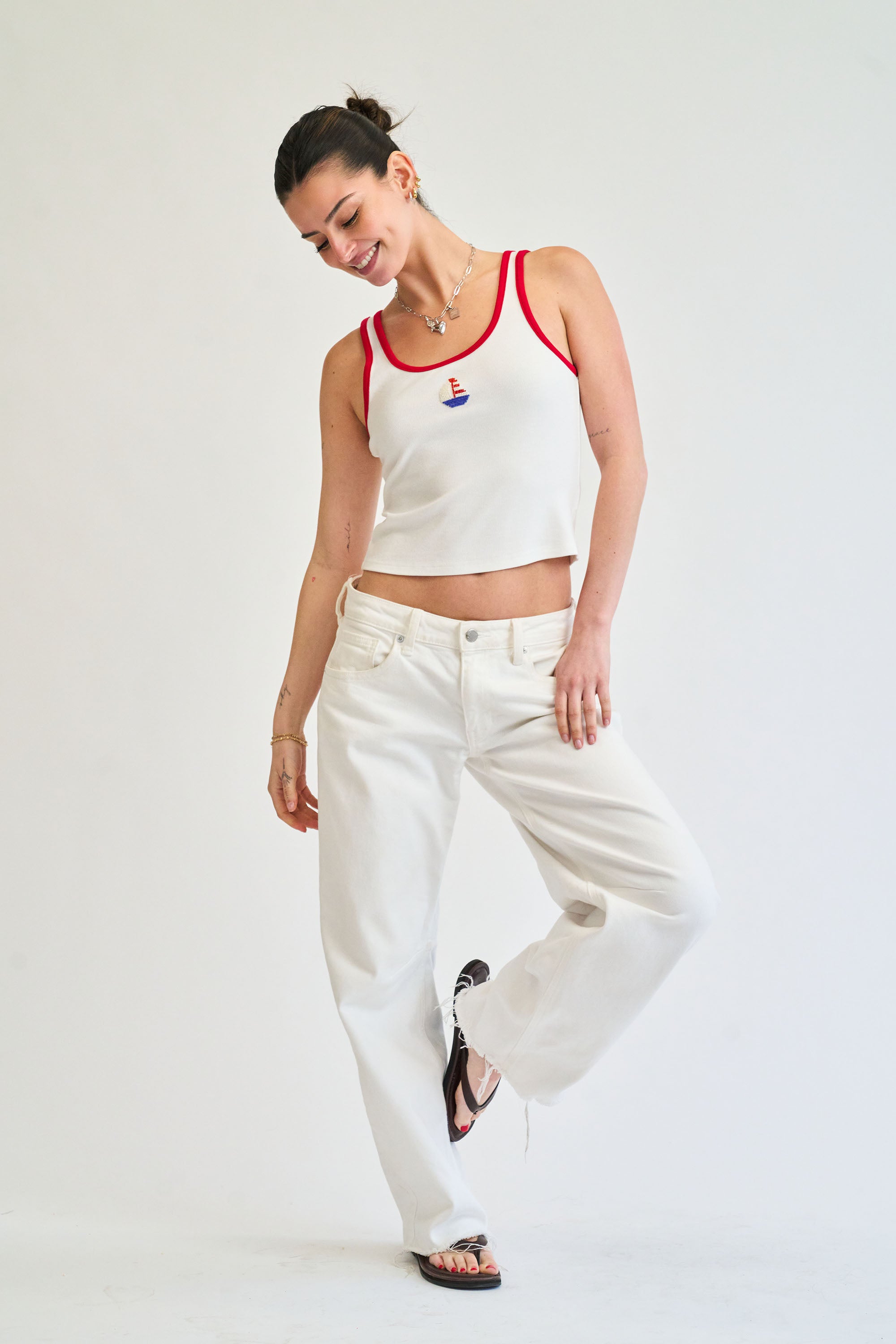 Woman wearing a white tank top with red trim and white pants on a plain background