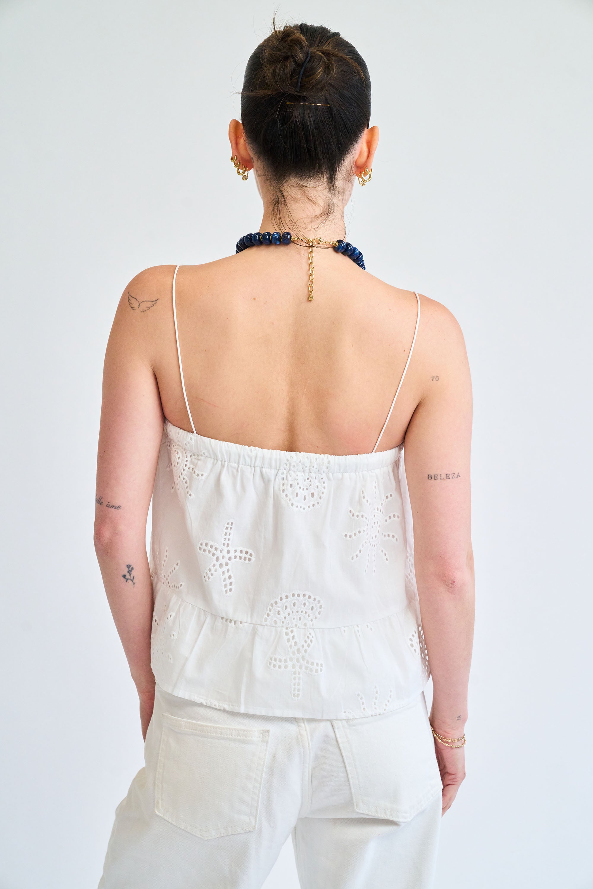 Person wearing a white lace top and white pants against a plain background