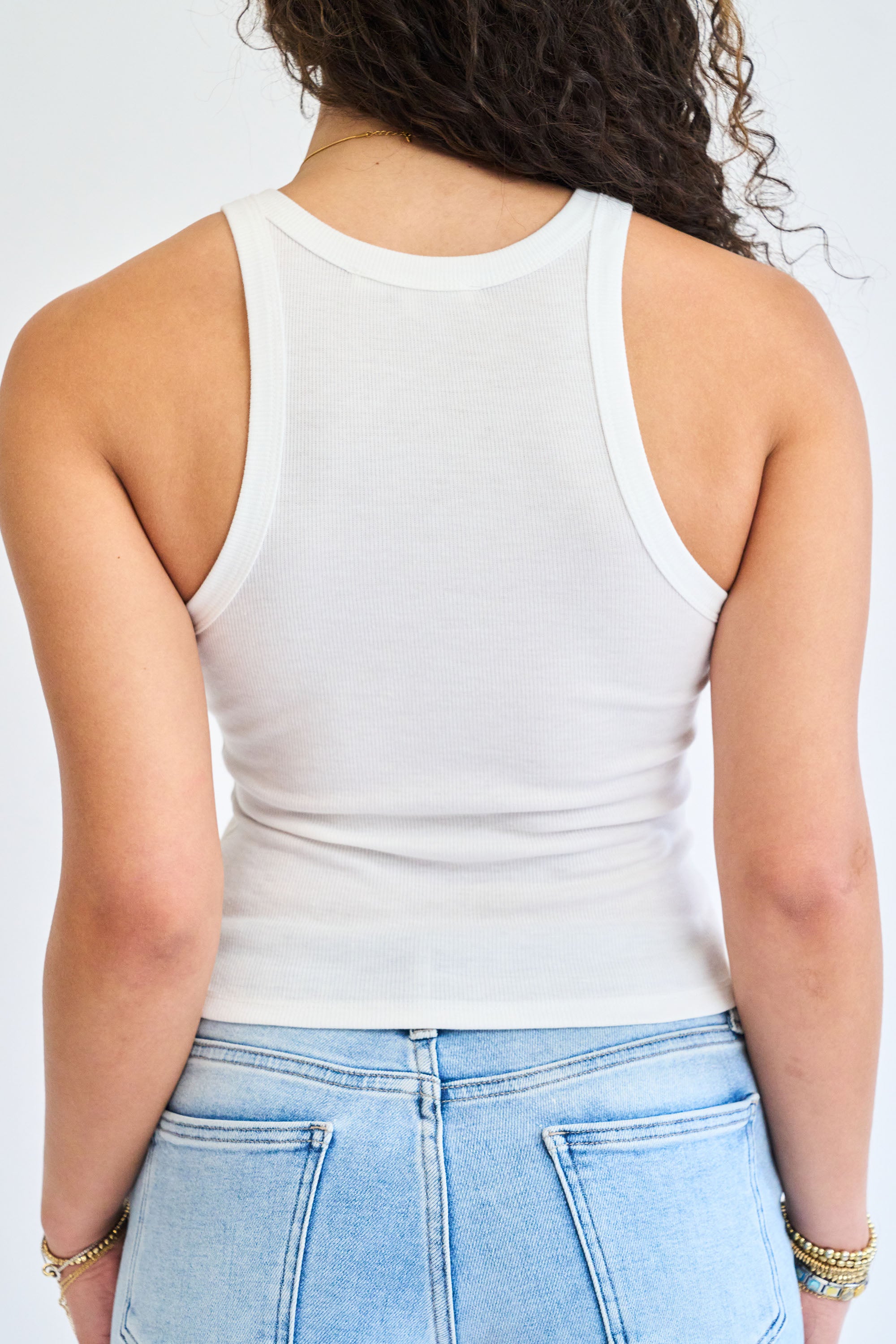 Person wearing a white tank top and light blue jeans on a plain background