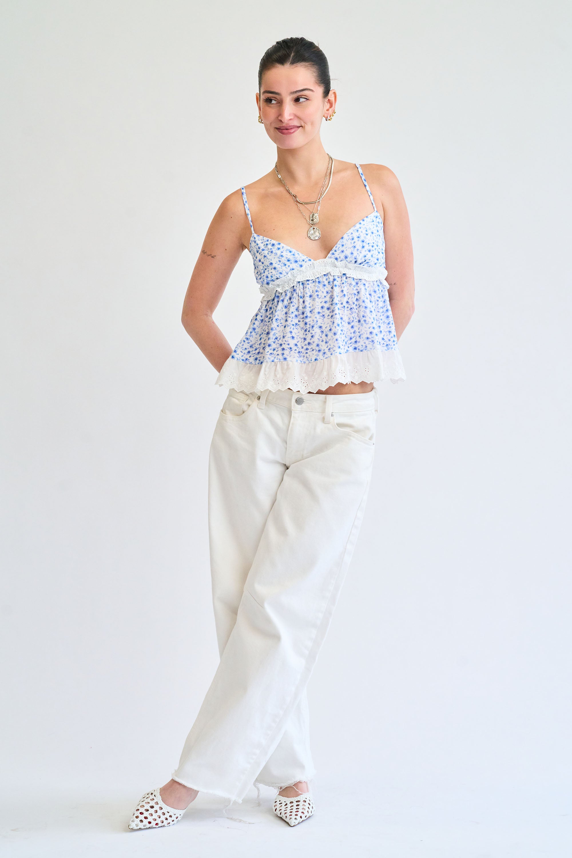 Woman wearing a floral top and white pants on a plain background
