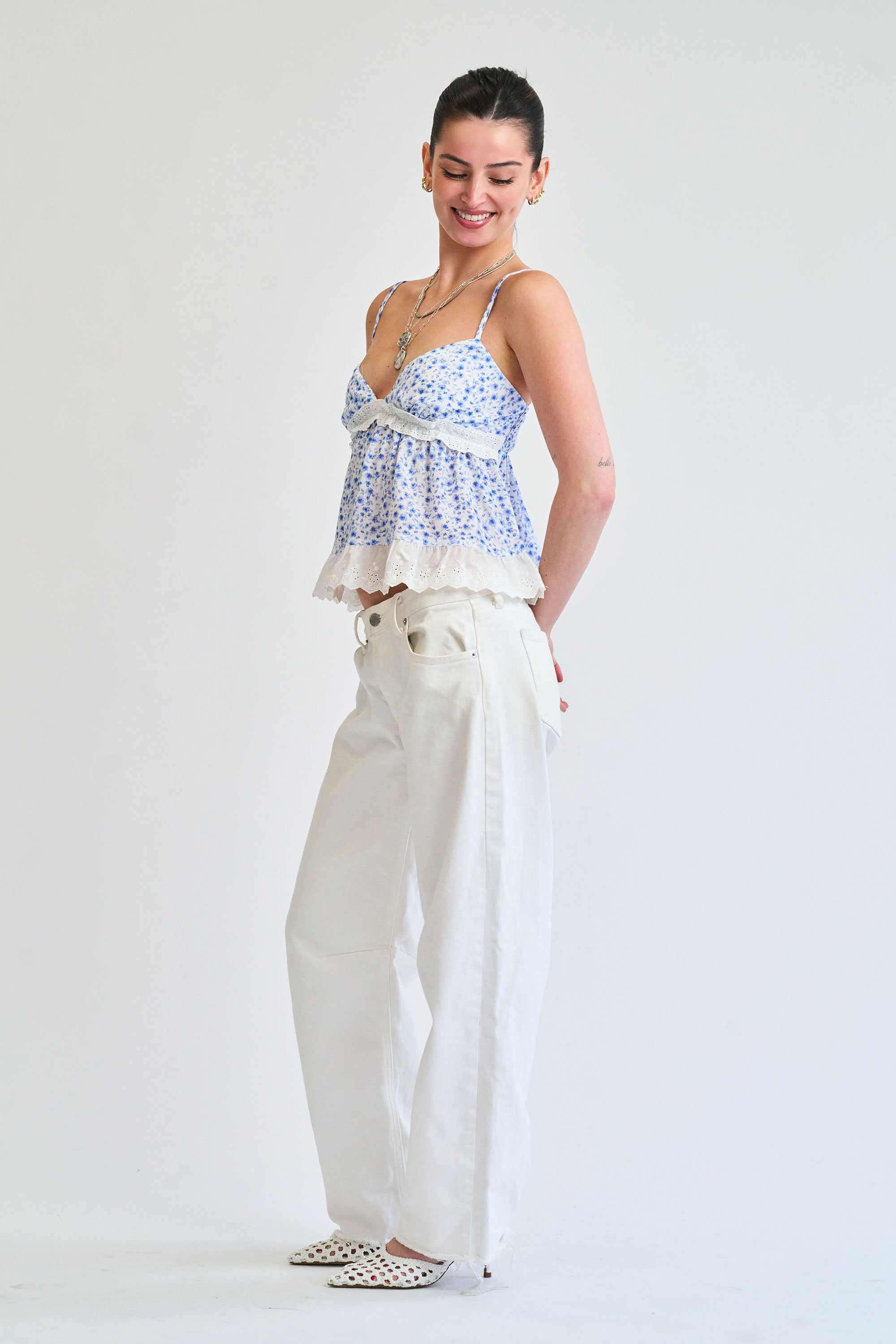 Woman wearing a blue patterned top and white pants on a white background