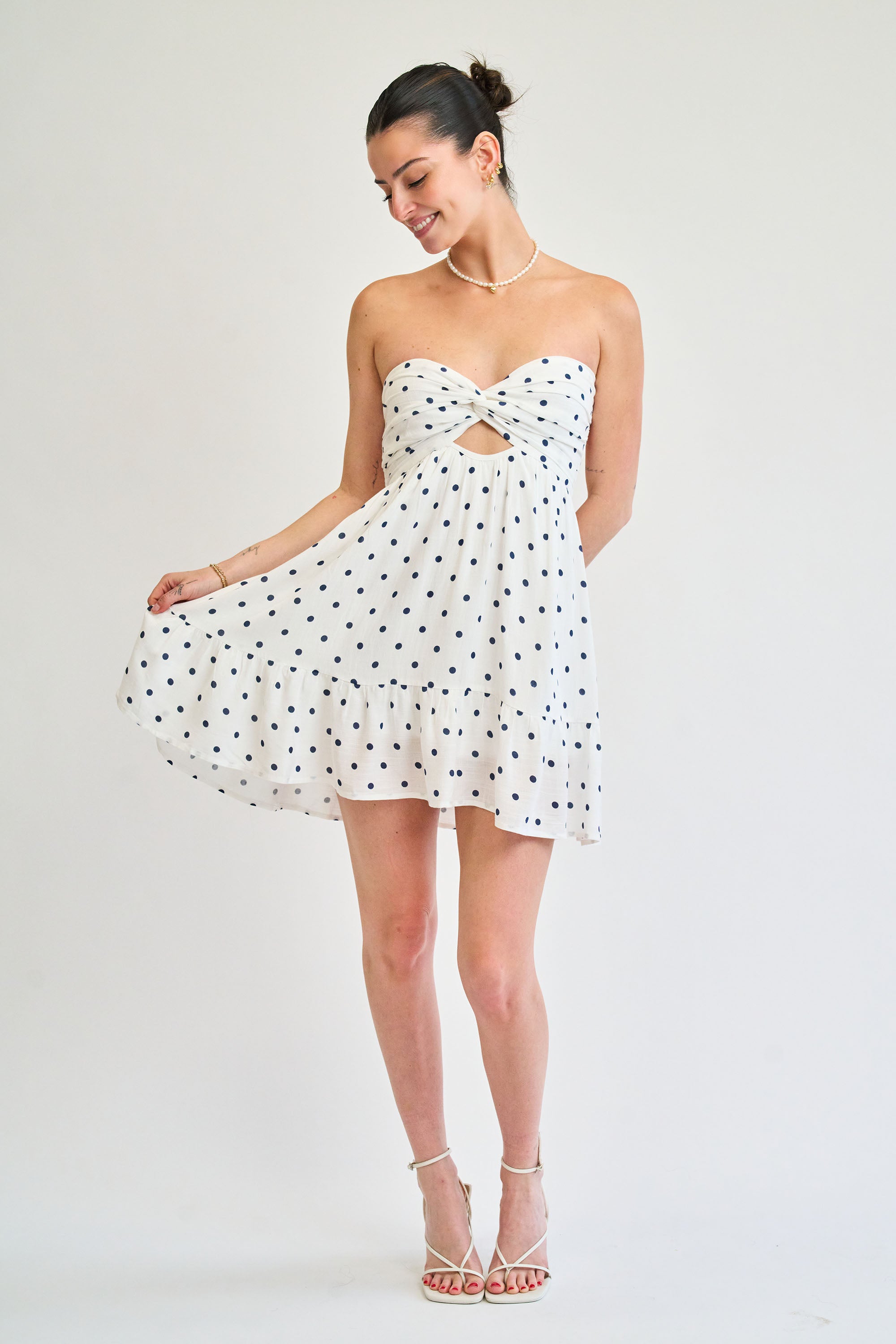 Woman wearing a white strapless dress with black polka dots on a plain background