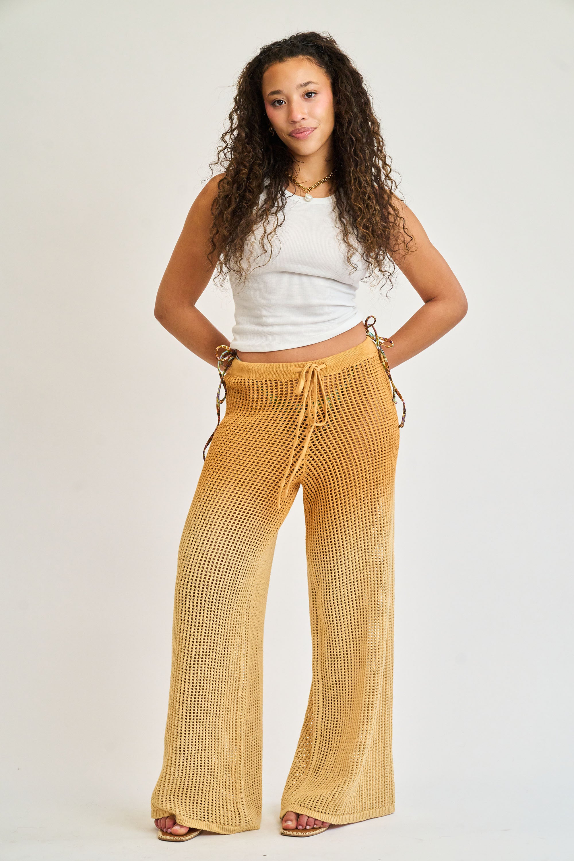 Woman wearing mustard yellow patterned pants and a white top on a plain background