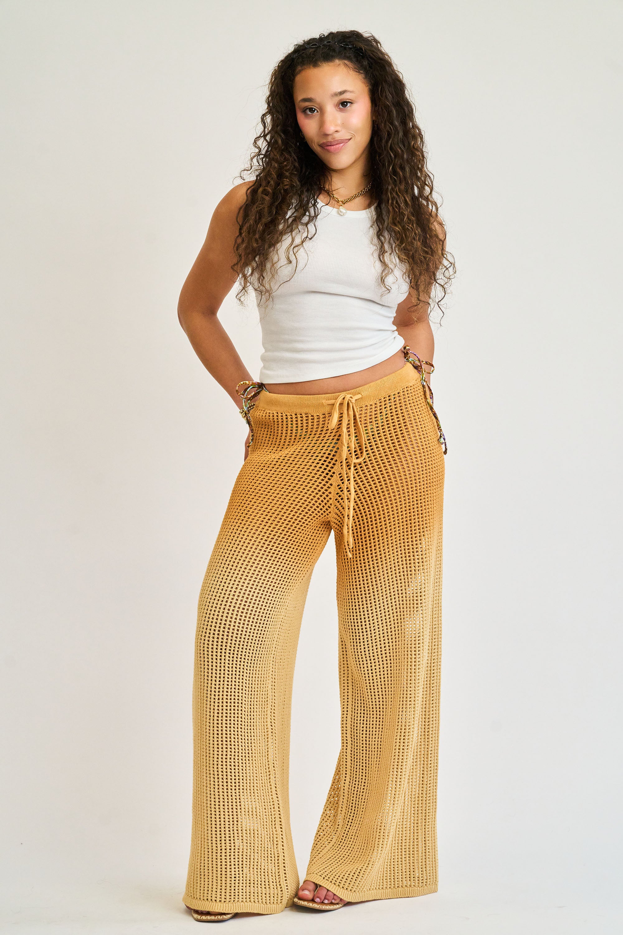 Woman wearing mustard yellow pants and a white top on a plain background
