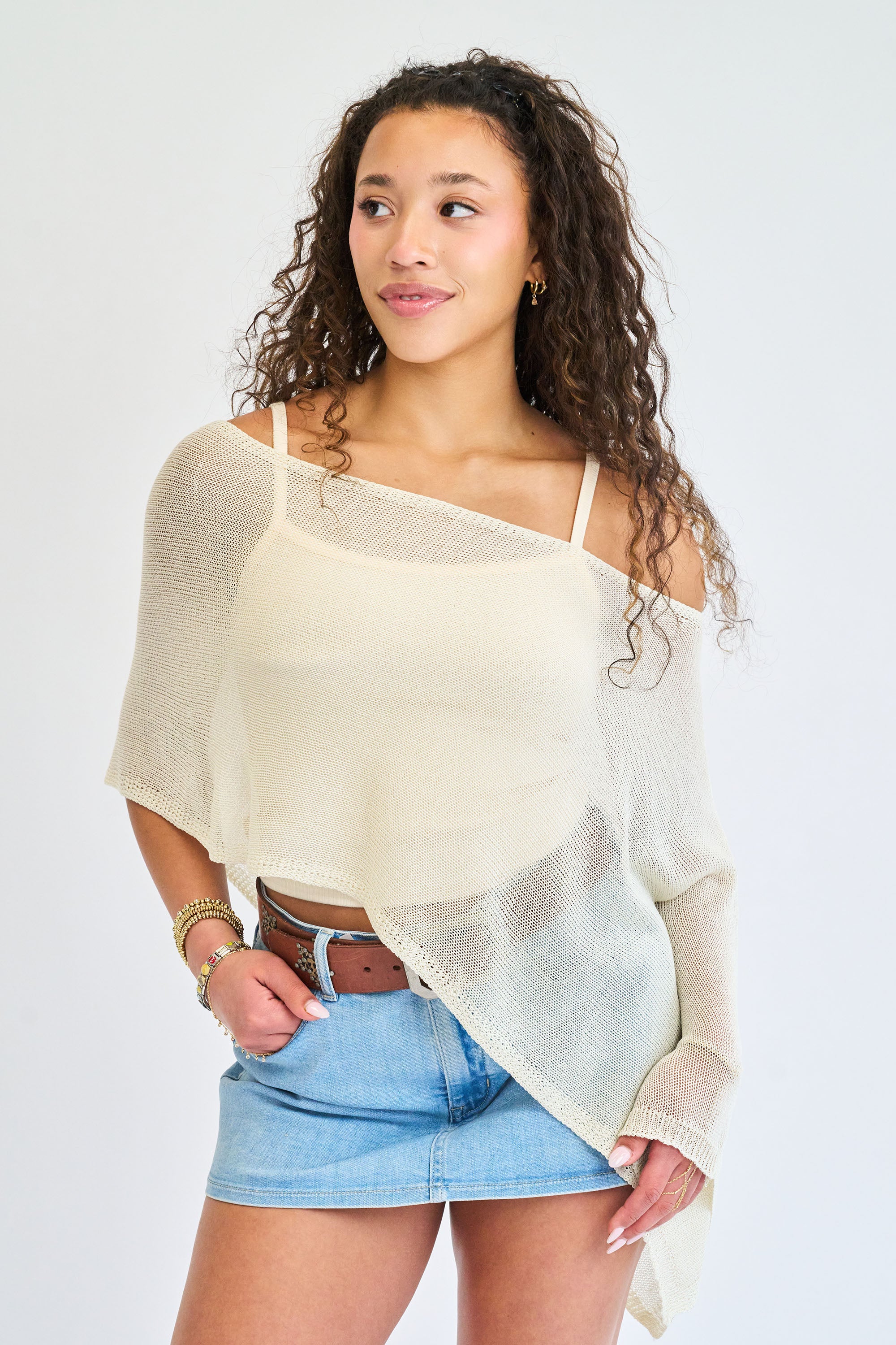 Woman wearing a beige off-shoulder top and denim shorts on a white background