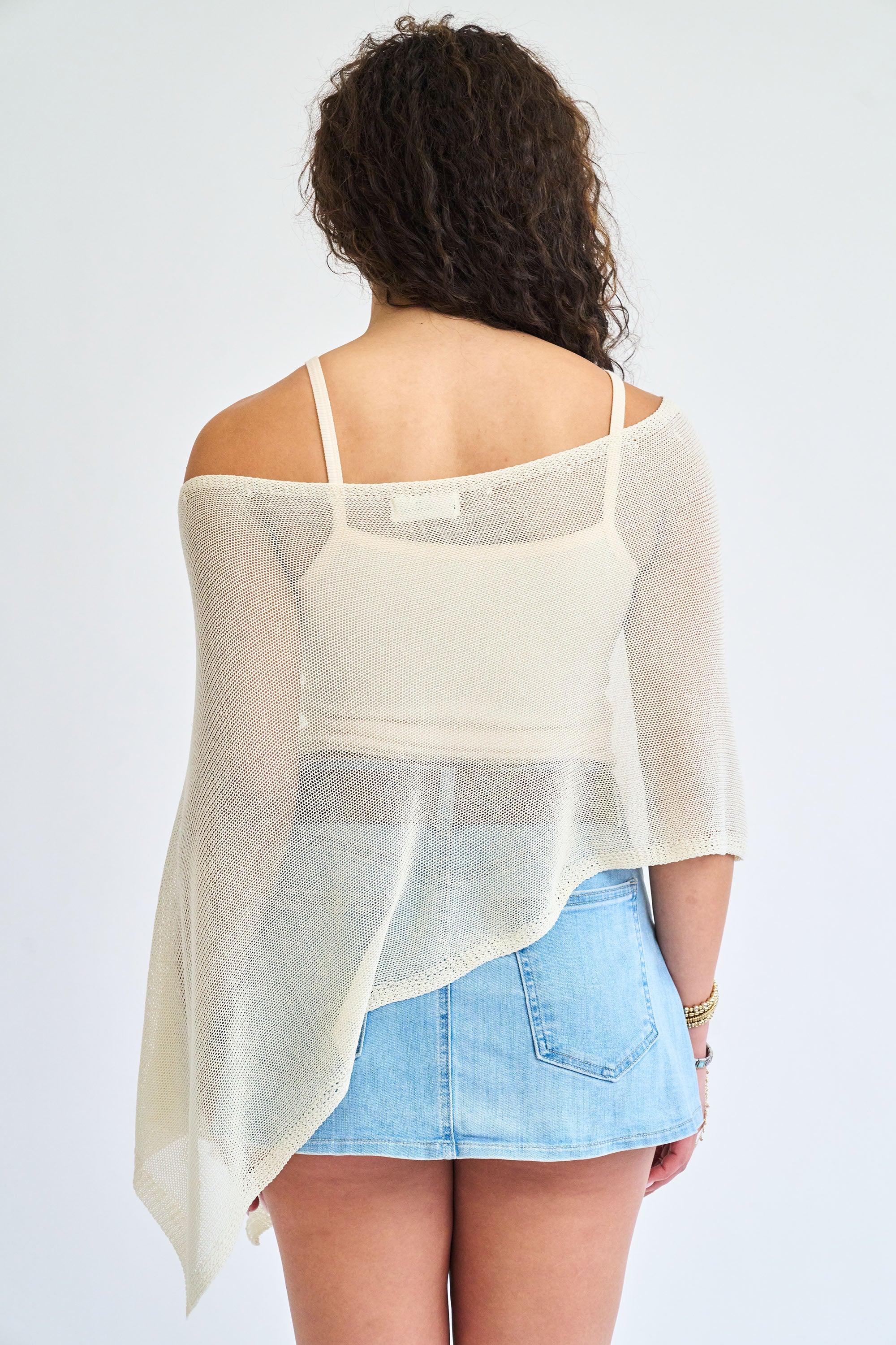 Woman wearing a sheer white top over a light blue skirt on a plain background