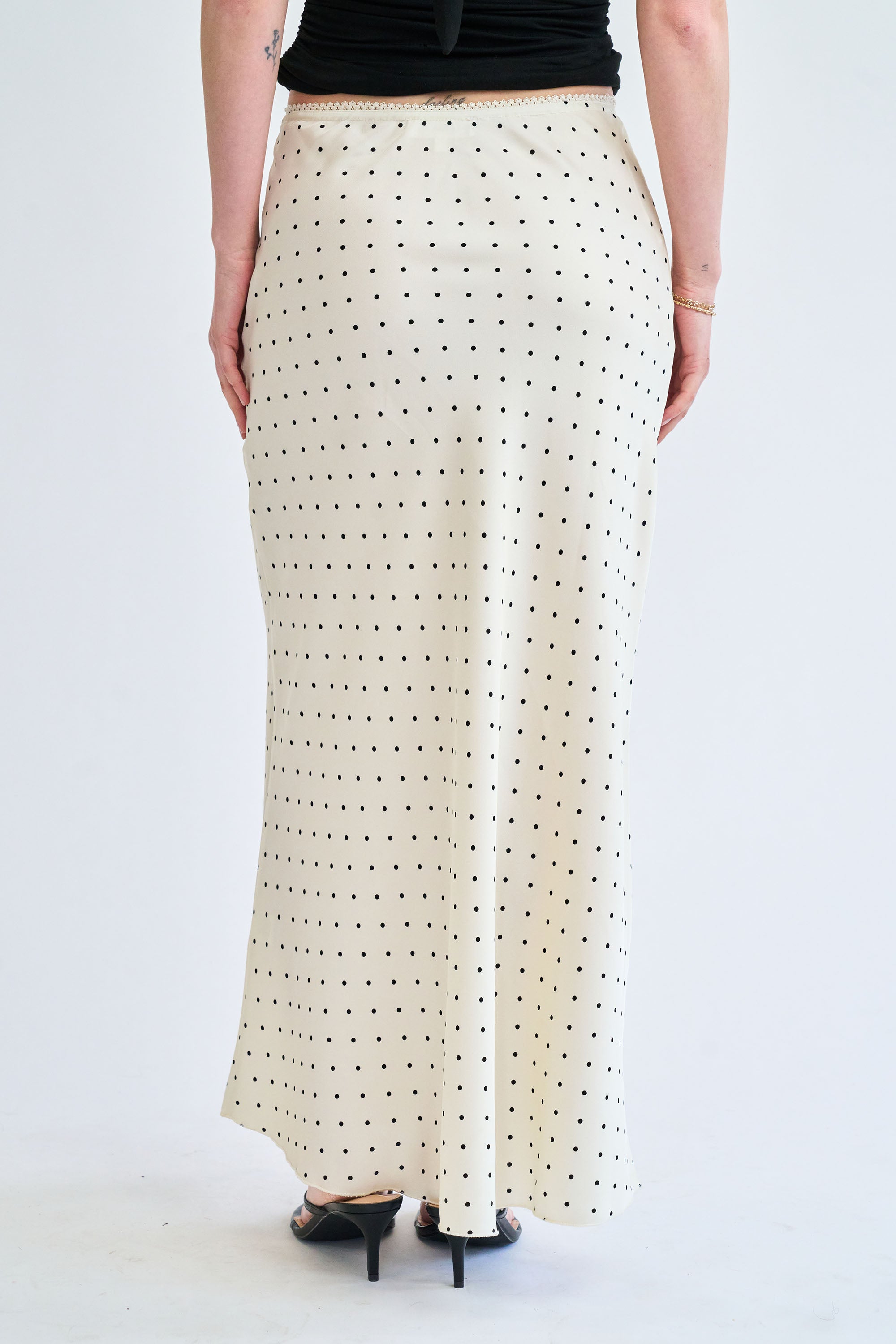 Person wearing a long, white skirt with black polka dots on a plain background