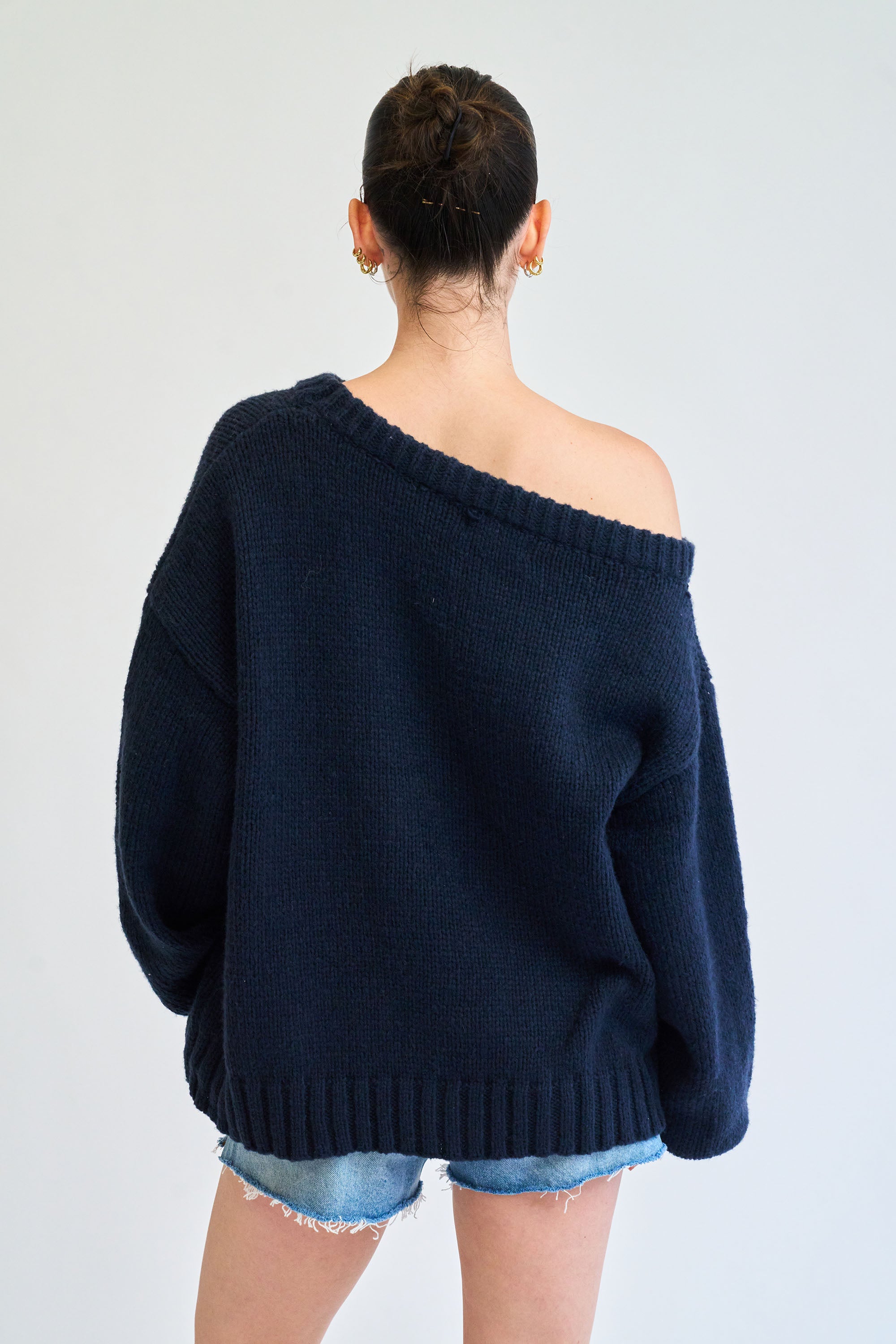 Person wearing a navy blue off-shoulder sweater on a plain background