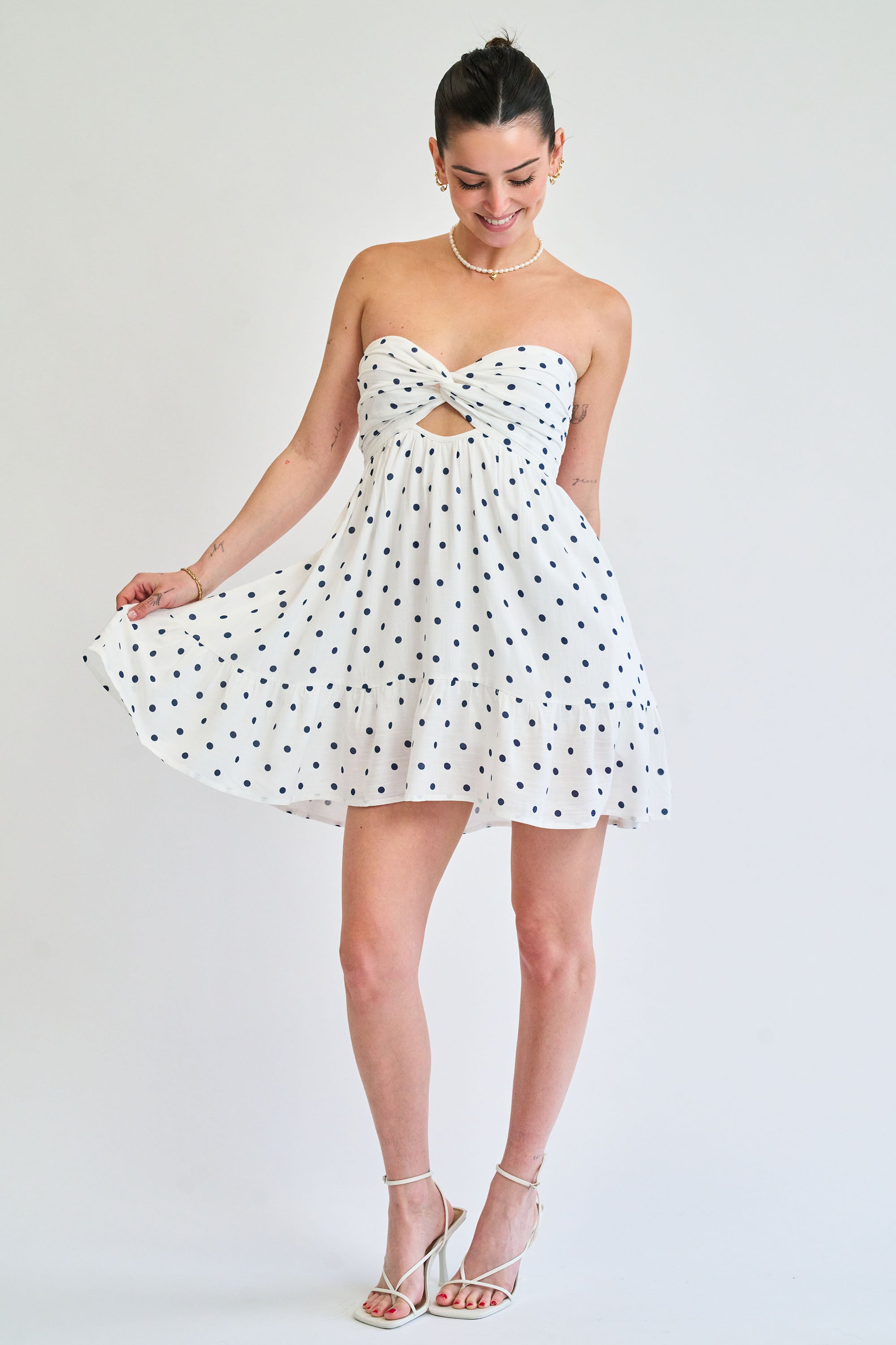 Woman wearing a white strapless dress with black polka dots on a plain background