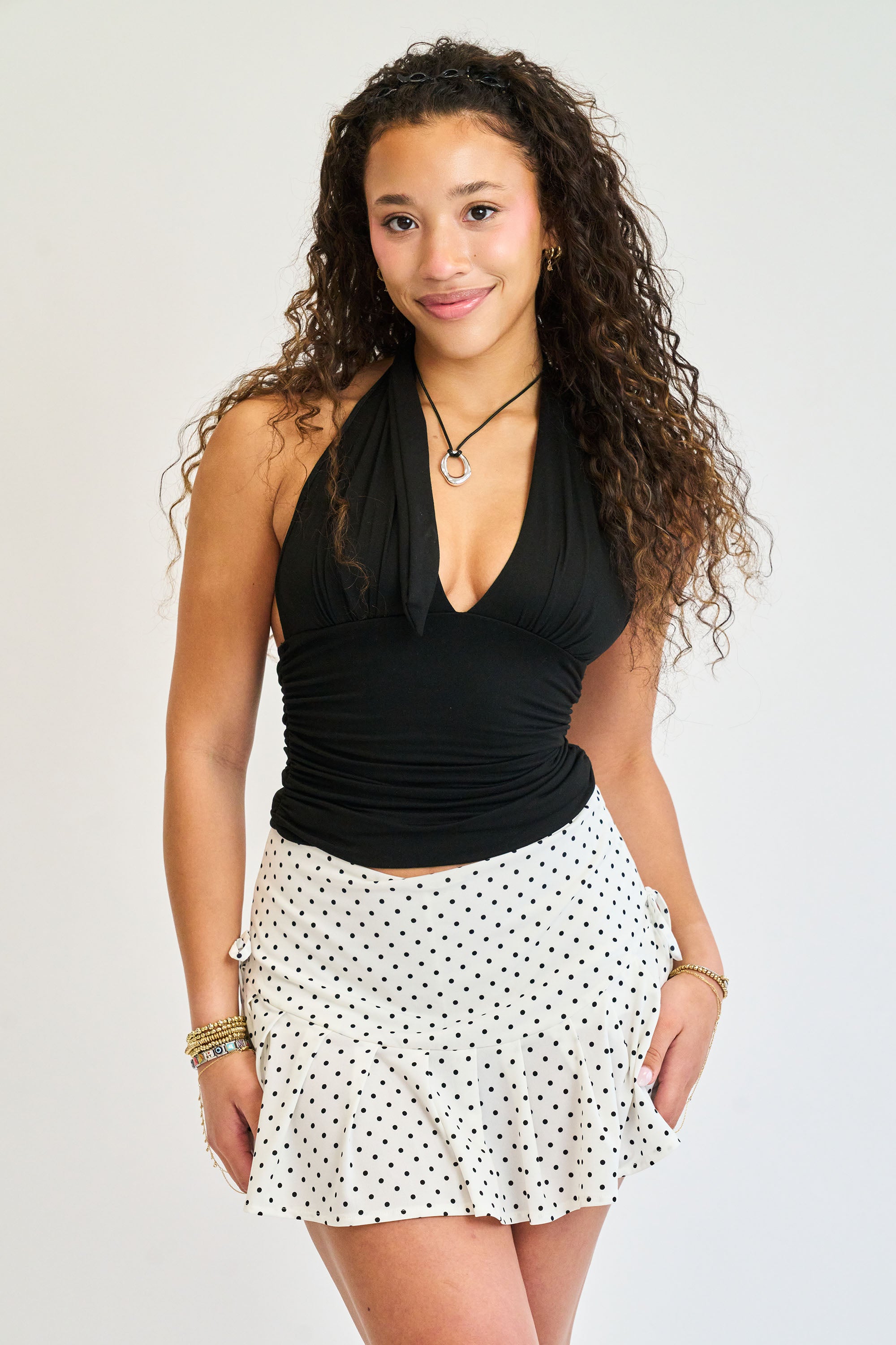 Woman wearing a black halter top and white polka dot skirt on a plain background
