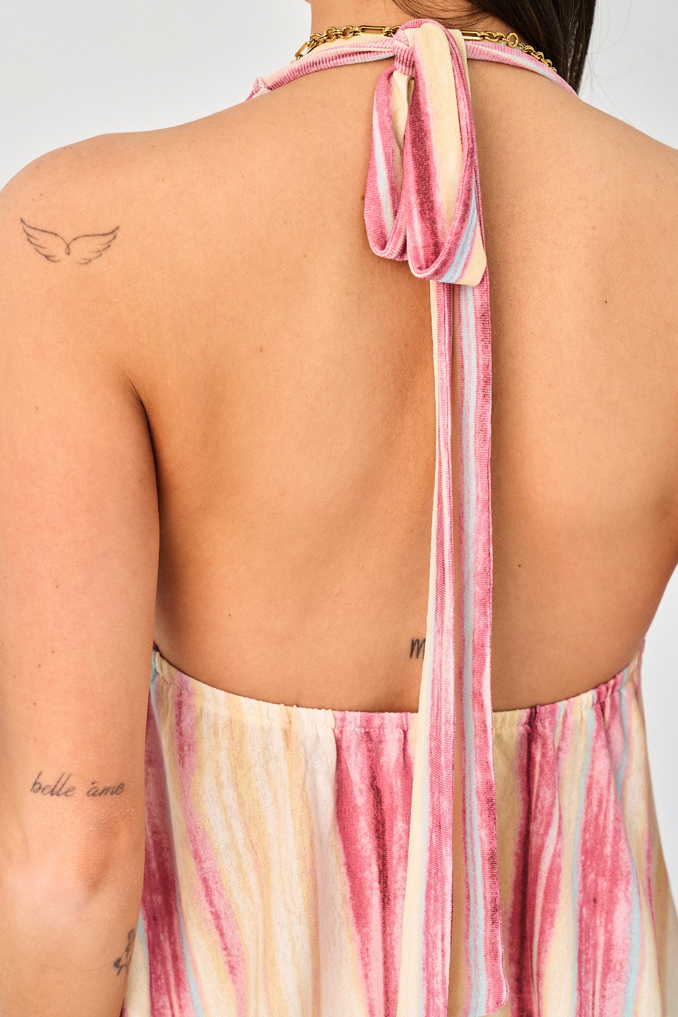 Back view of a person wearing a pink and white striped halter top with a blurred background