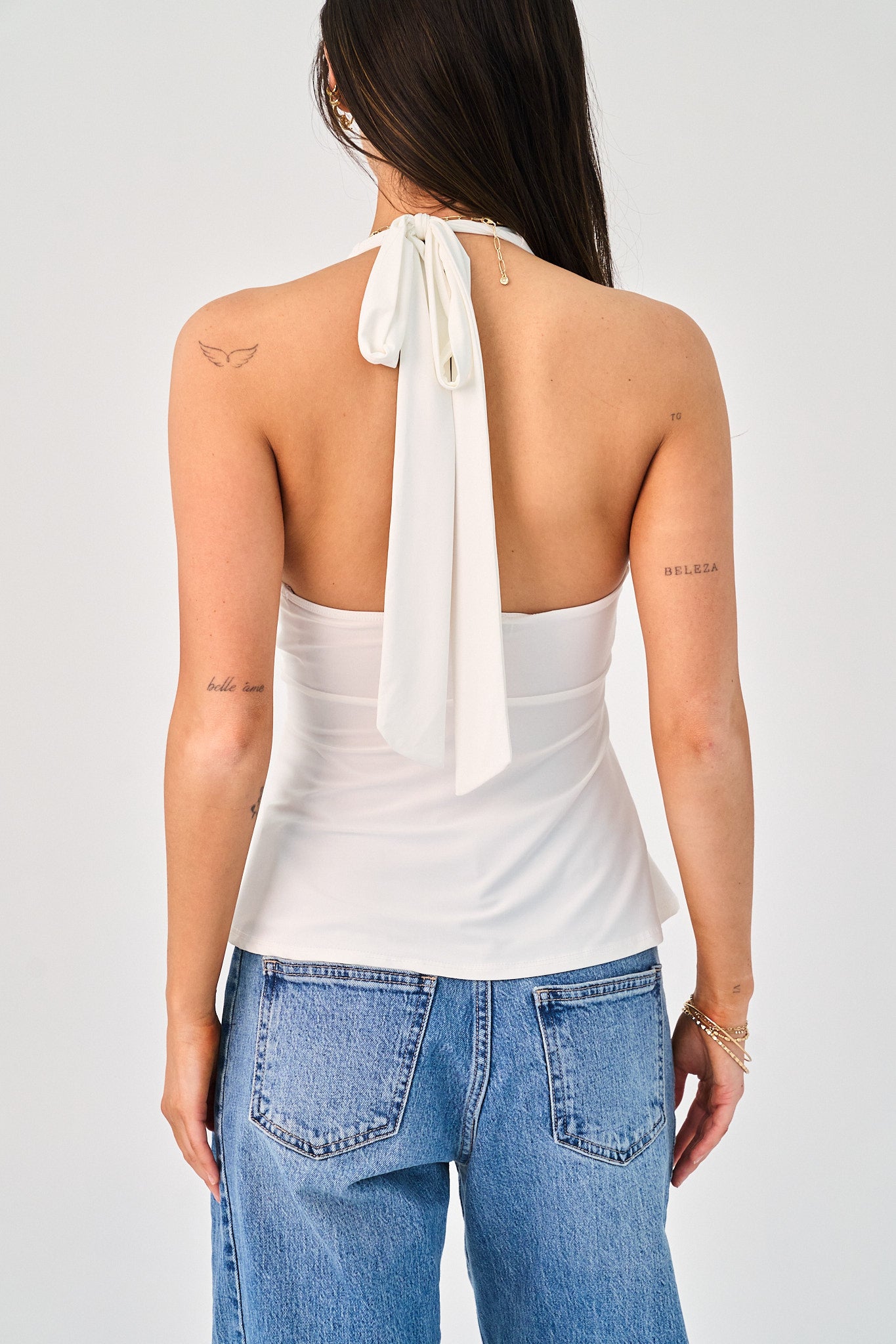 Woman wearing a white halter top with a bow detail and blue jeans on a plain background