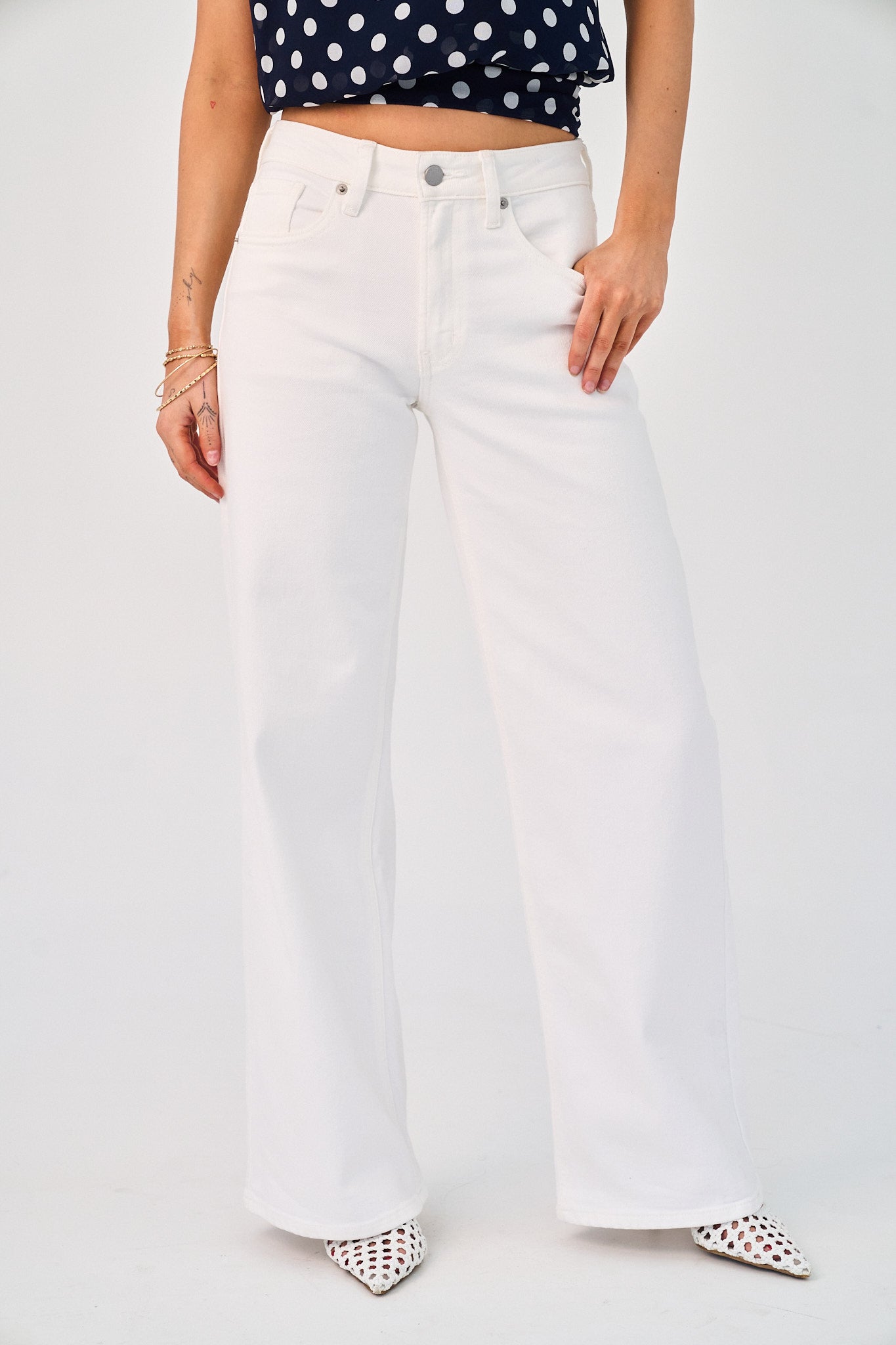 Person wearing white jeans and a polka dot top on a plain background