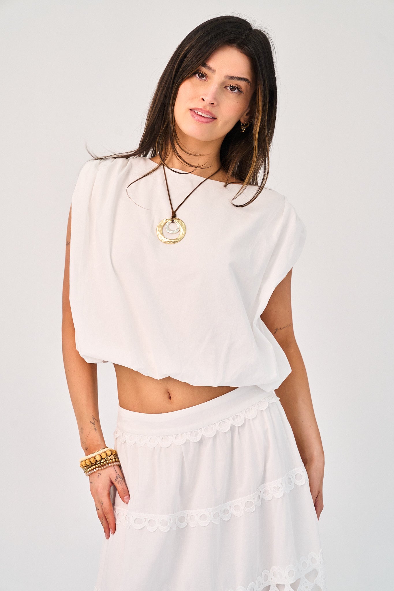 Woman wearing a white outfit with a necklace on a plain background