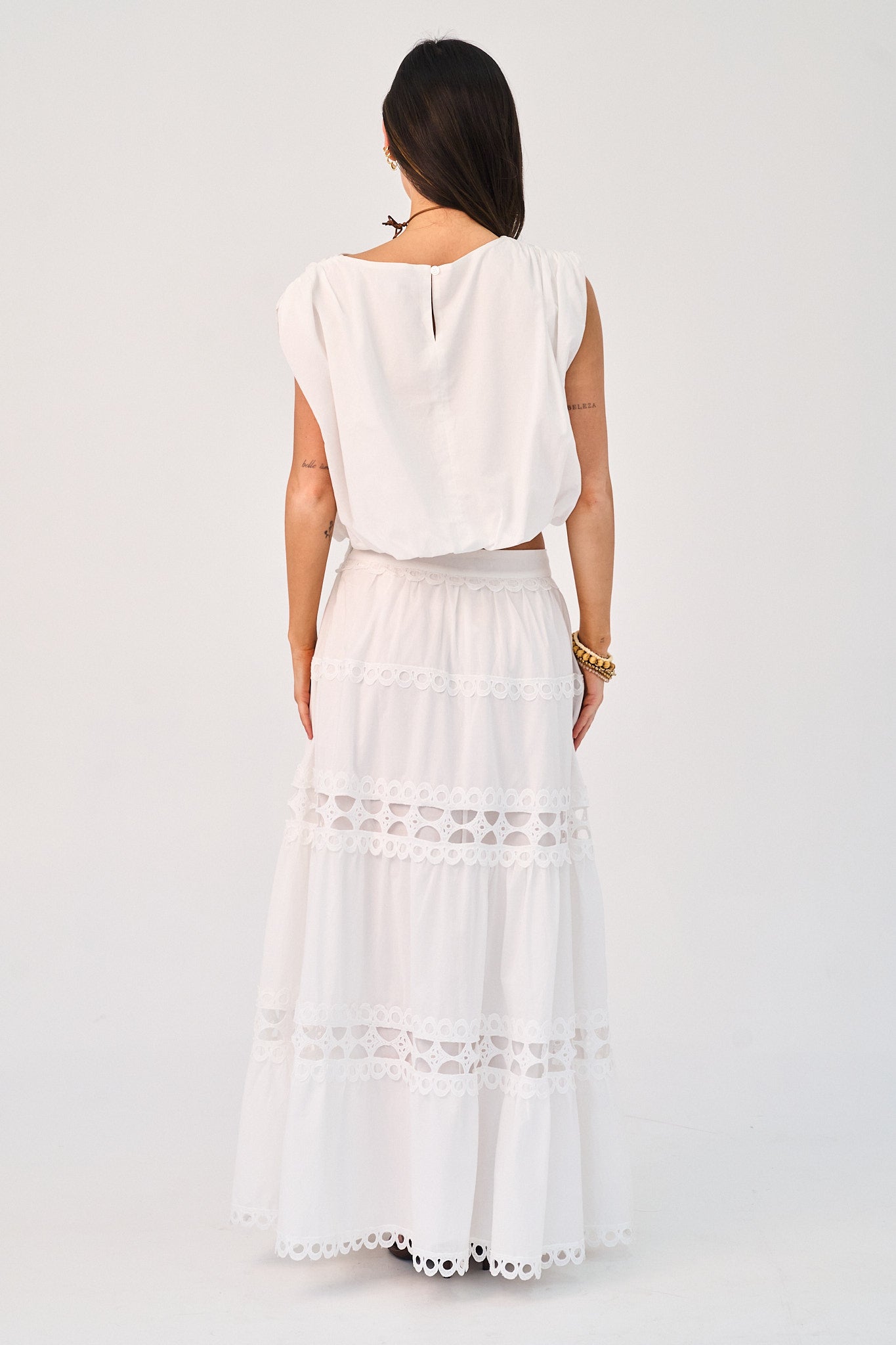 Woman wearing a white sleeveless top and white lace-trimmed skirt on a plain background