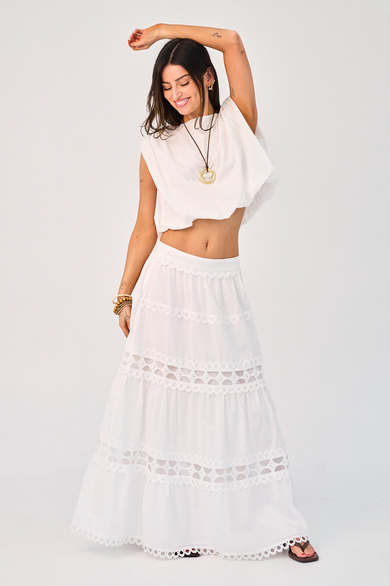Woman wearing a white outfit with a long skirt and top on a plain background