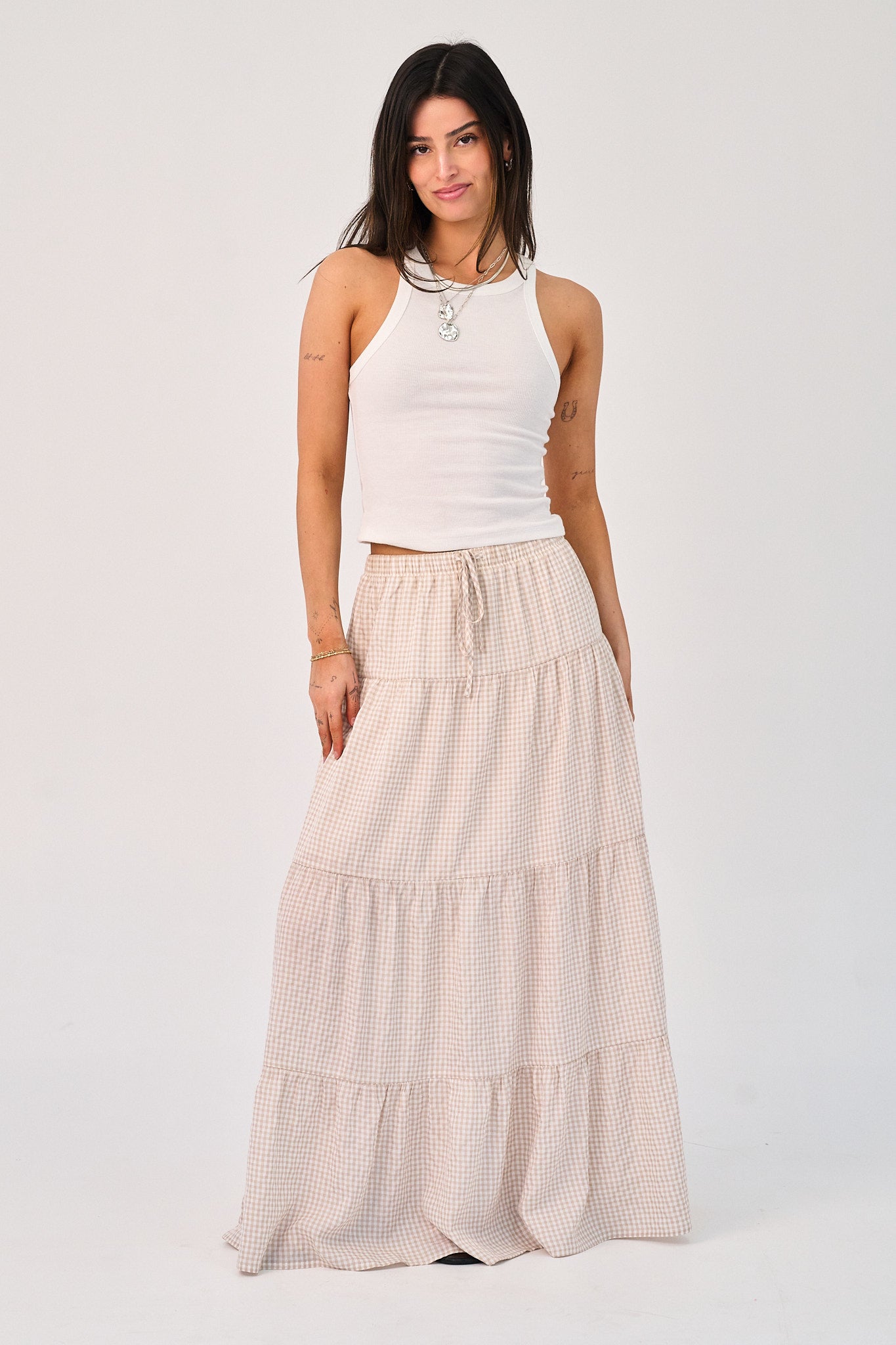 Woman wearing a white sleeveless top and beige tiered skirt on a white background