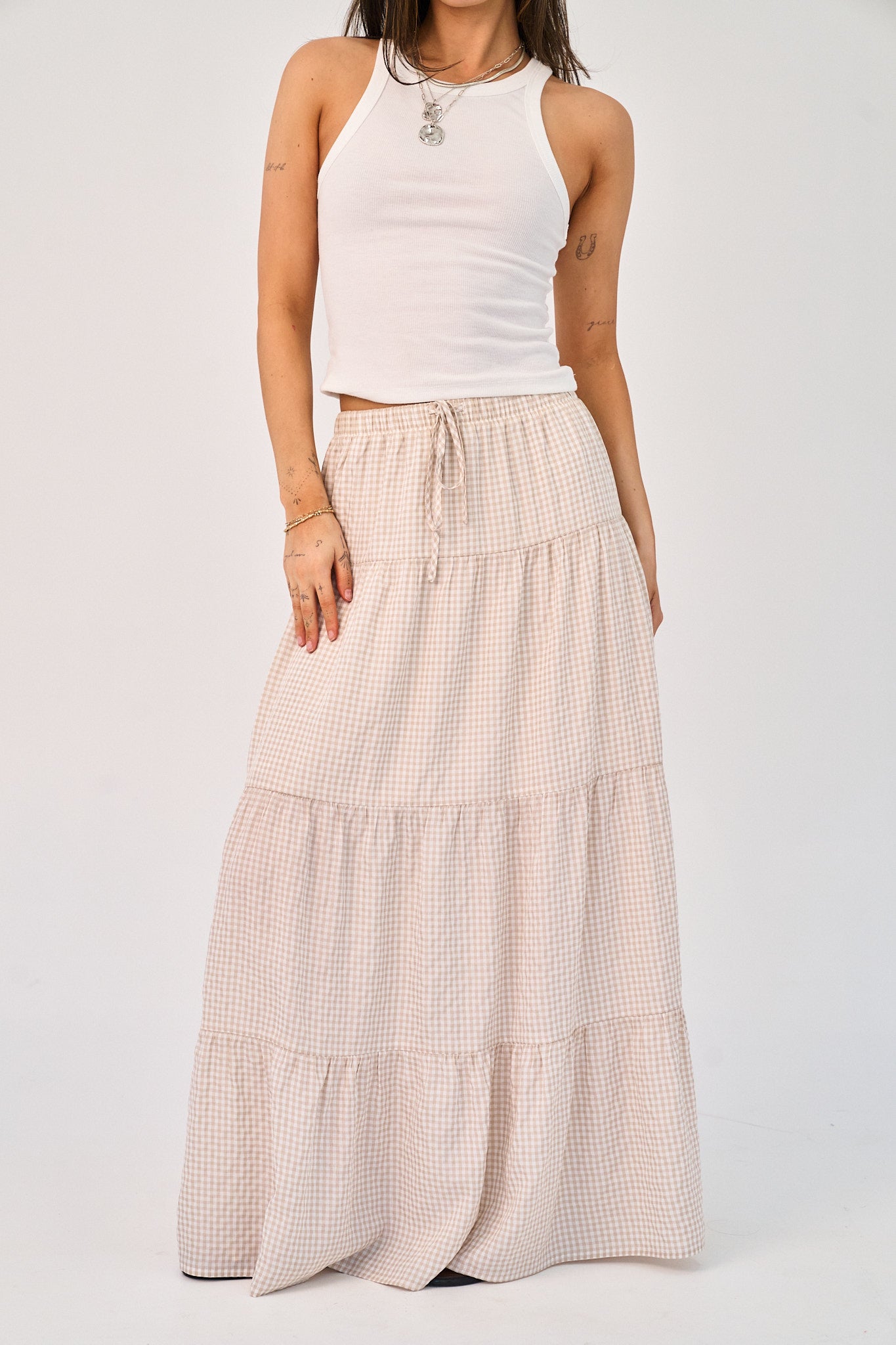 Woman wearing a white tank top and tiered checkered skirt on a white background