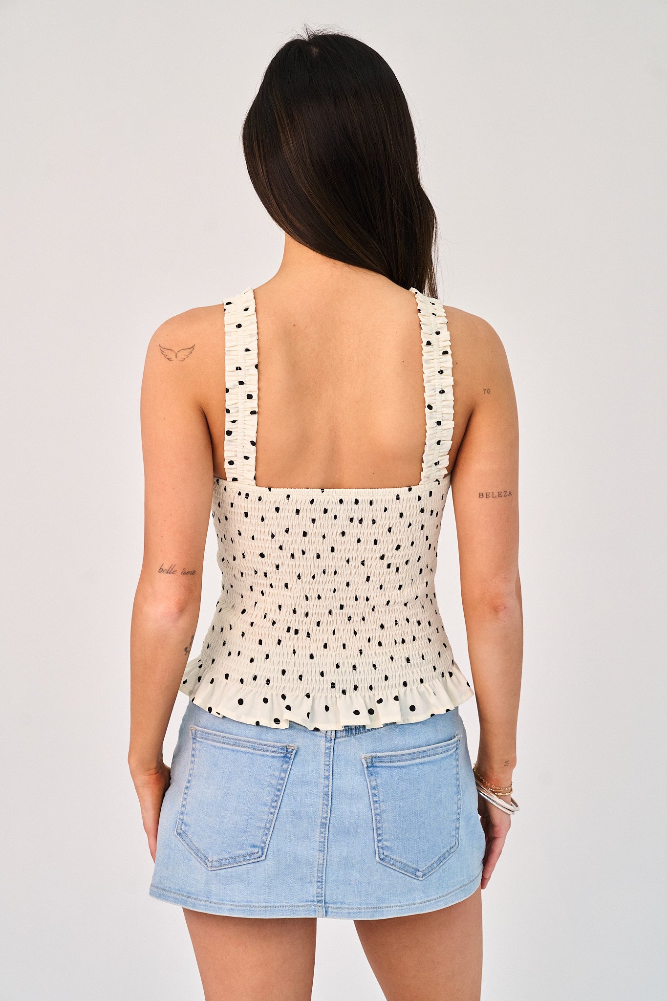 Woman wearing a polka dot top and denim skirt on a plain background