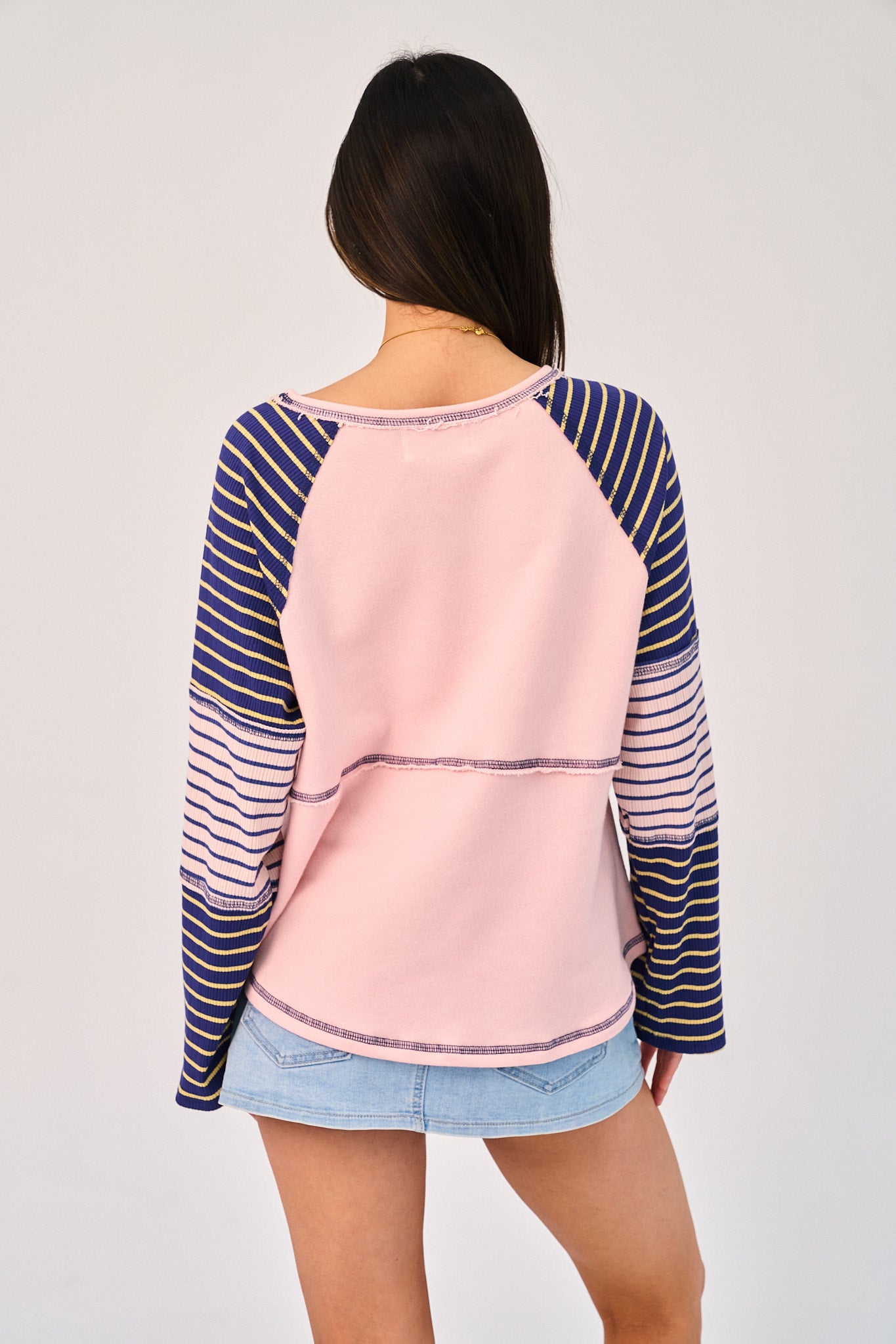 Person wearing a pink and blue striped long-sleeve top with a plain background