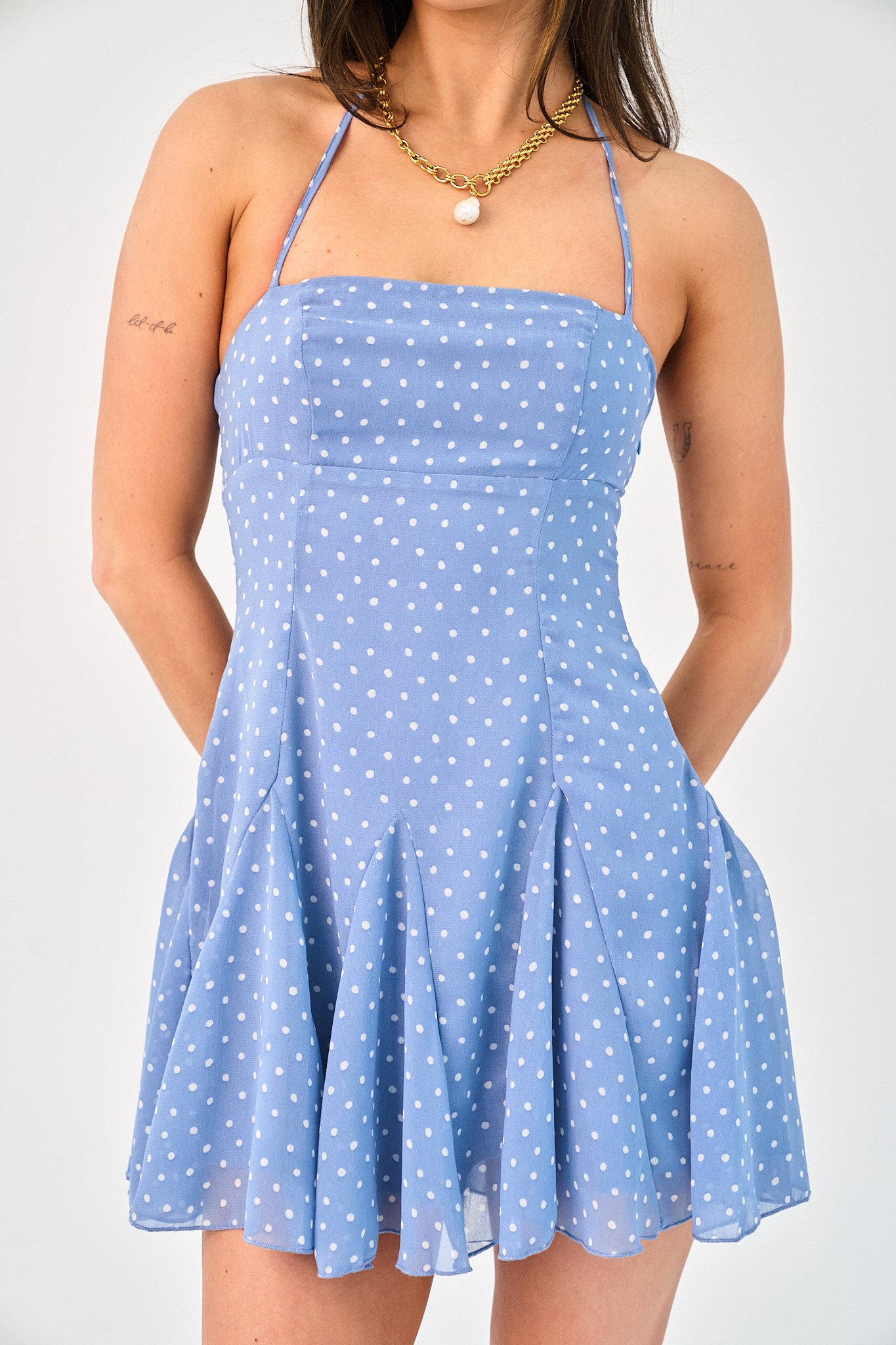 Woman wearing a blue polka dot dress against a plain background