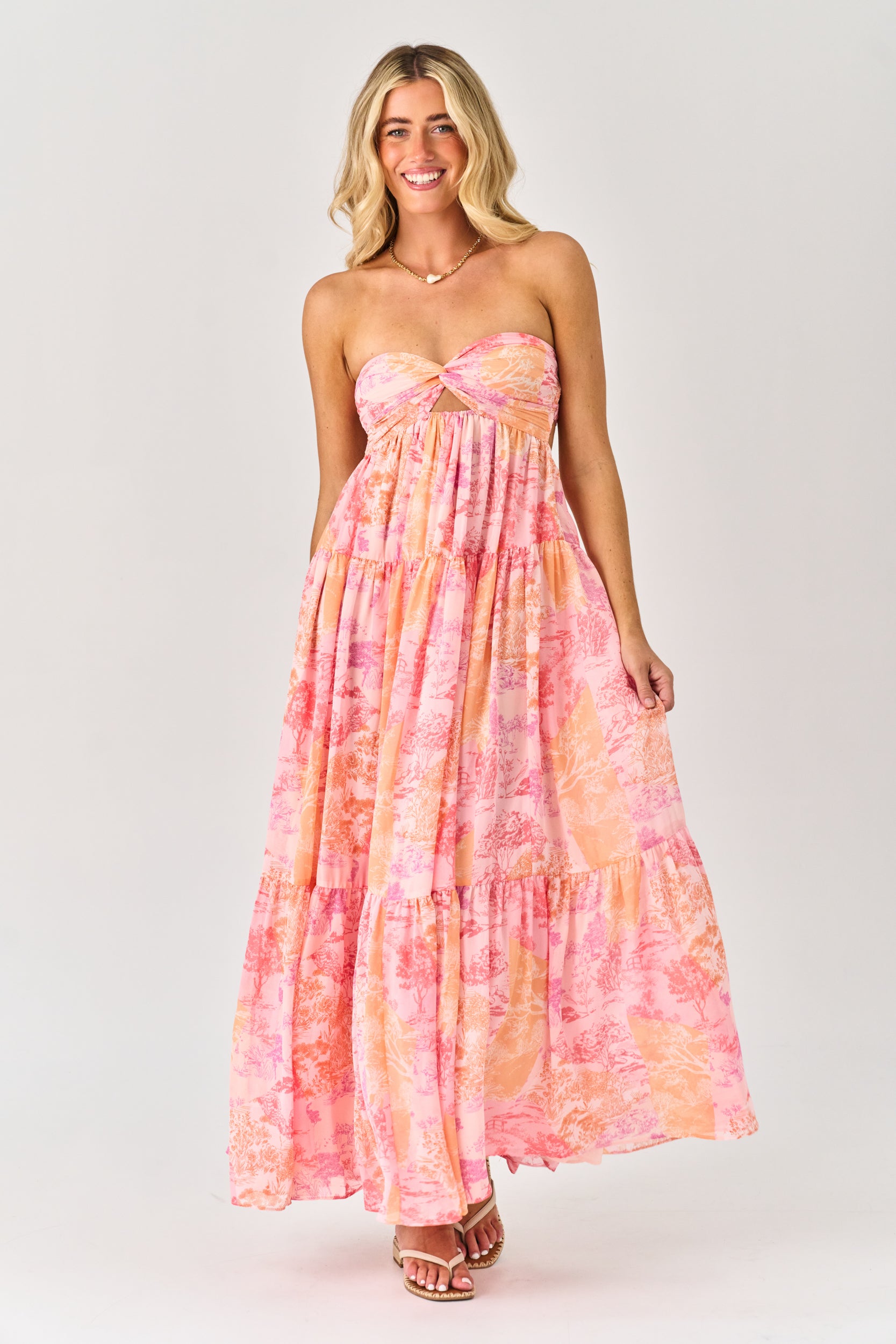 Woman wearing a strapless, tie-dye pink and orange dress on a white background