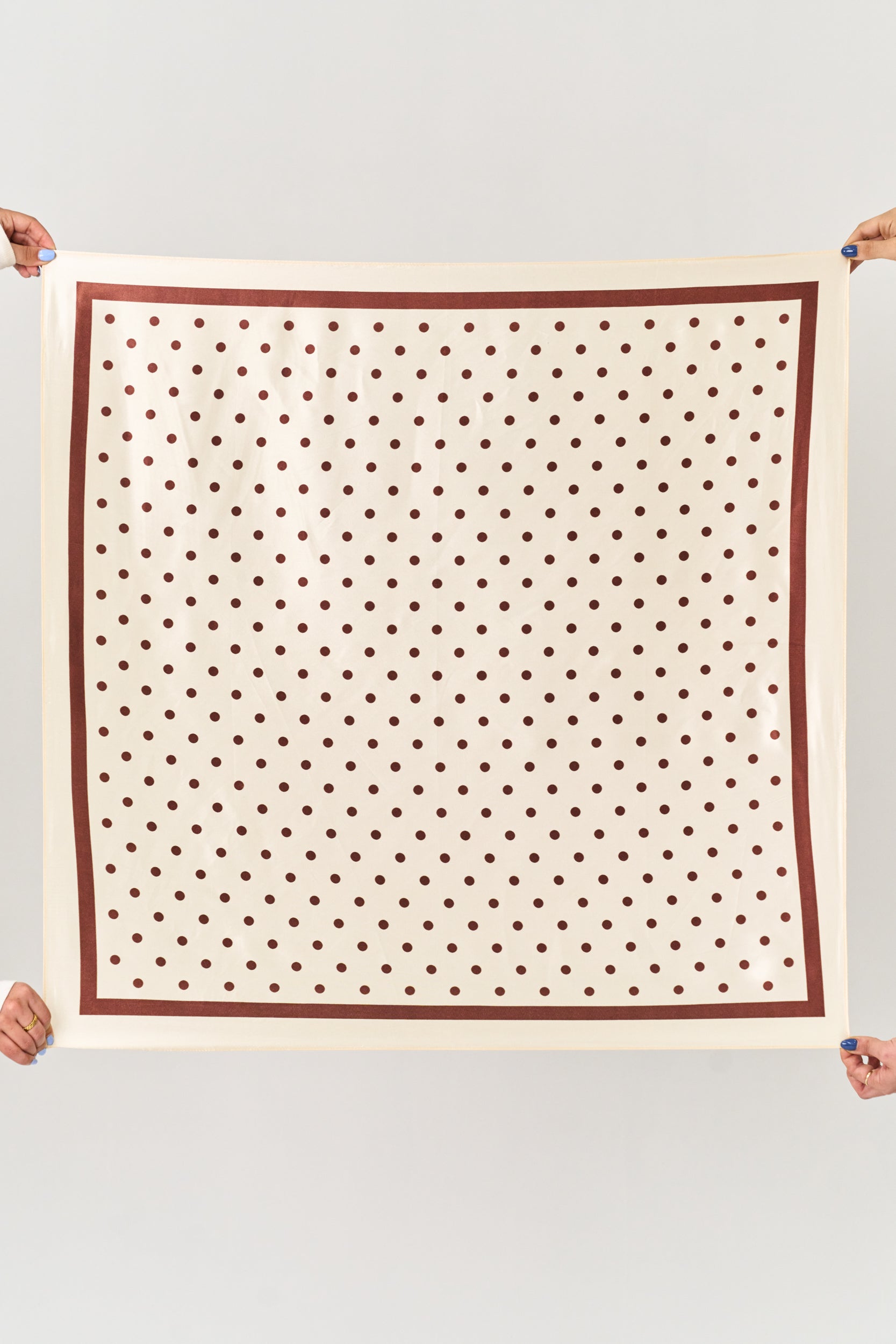 Person holding a square scarf with brown polka dots on a white background